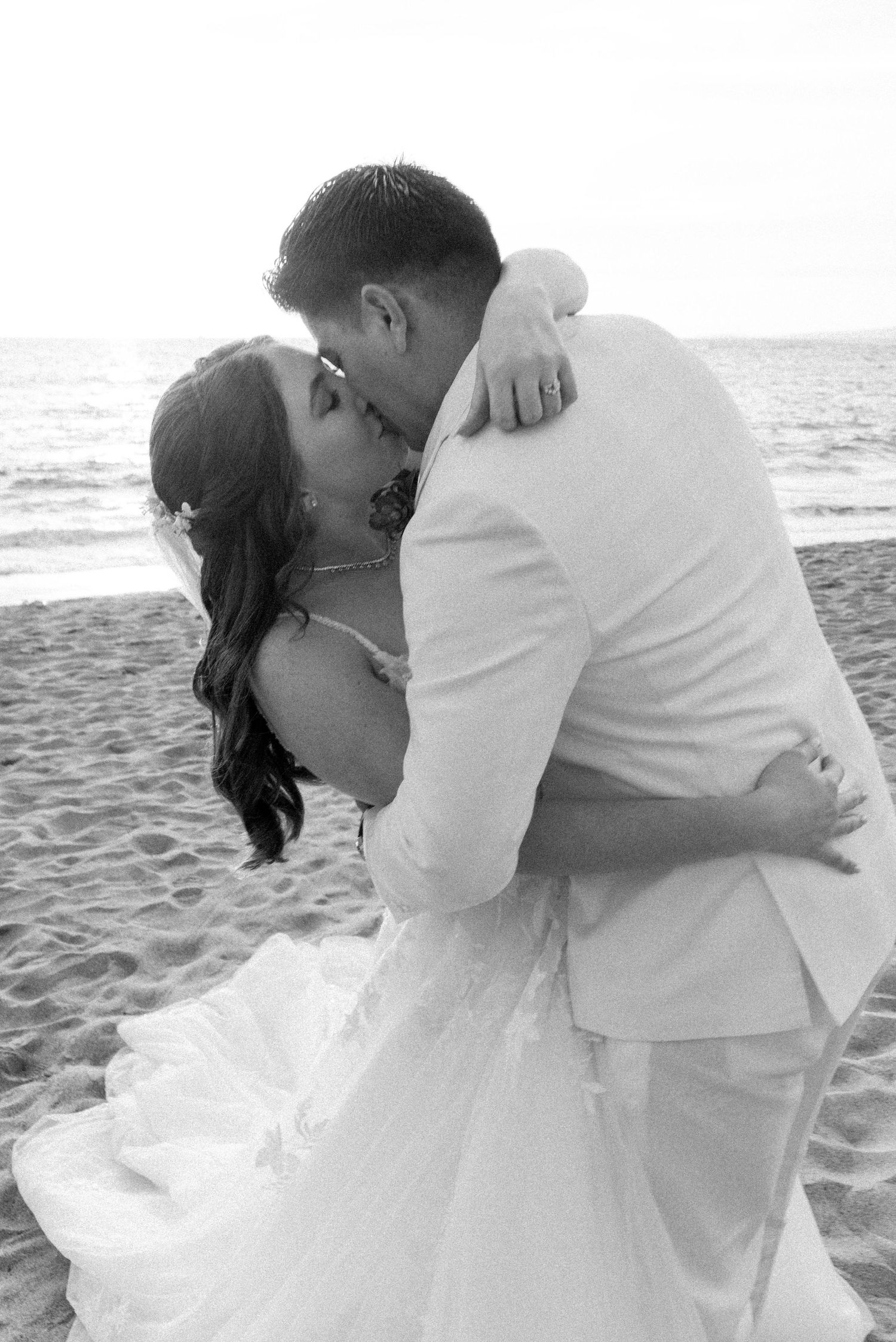 A black and white portrait of a wedding couple's intimate embrace on a sandy beach.