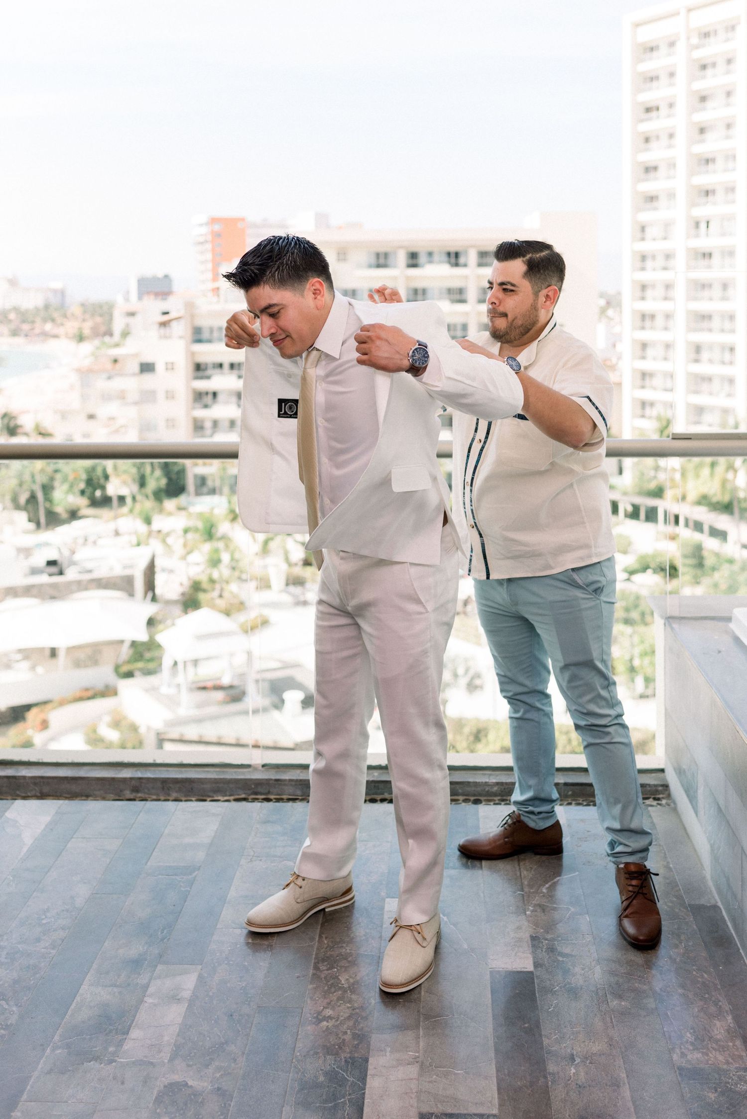 Two groomsmen in light colored suits helping with final wedding preparations on a rooftop.