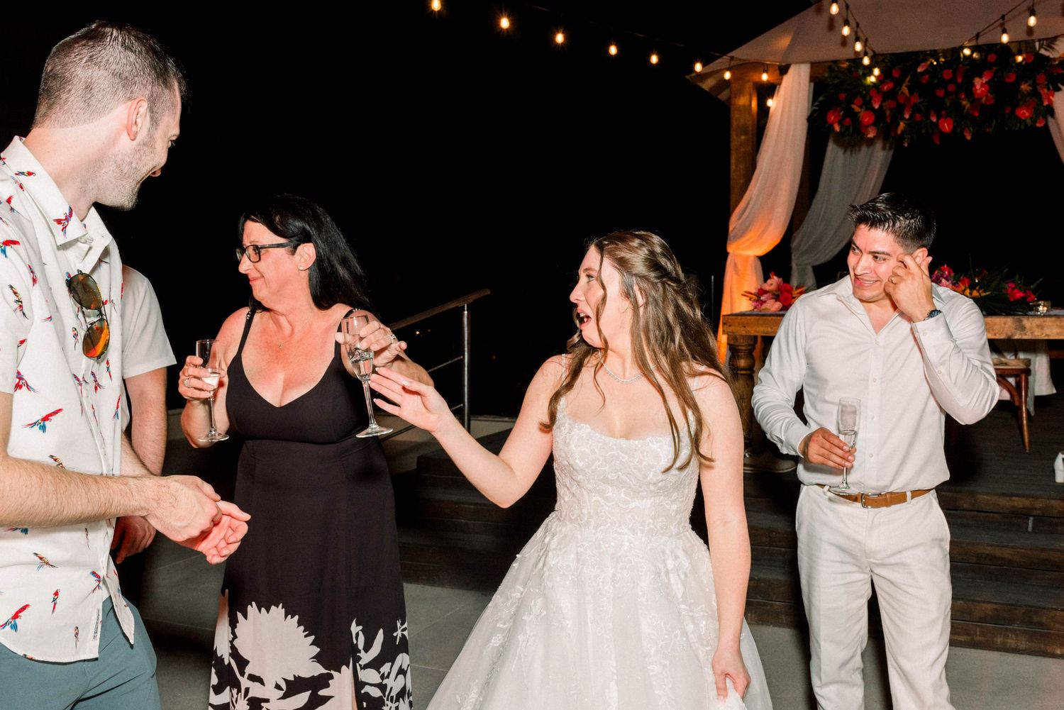 Wedding guests and the bride dancing together under string lights at an outdoor reception.