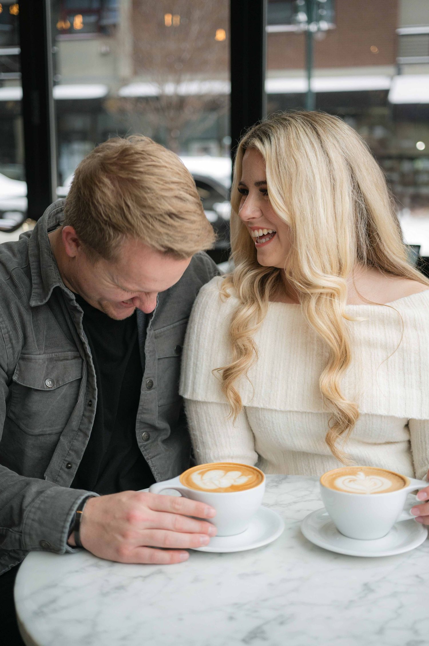 A couple shares a cozy moment at a cafe over cappuccinos at a marble table.