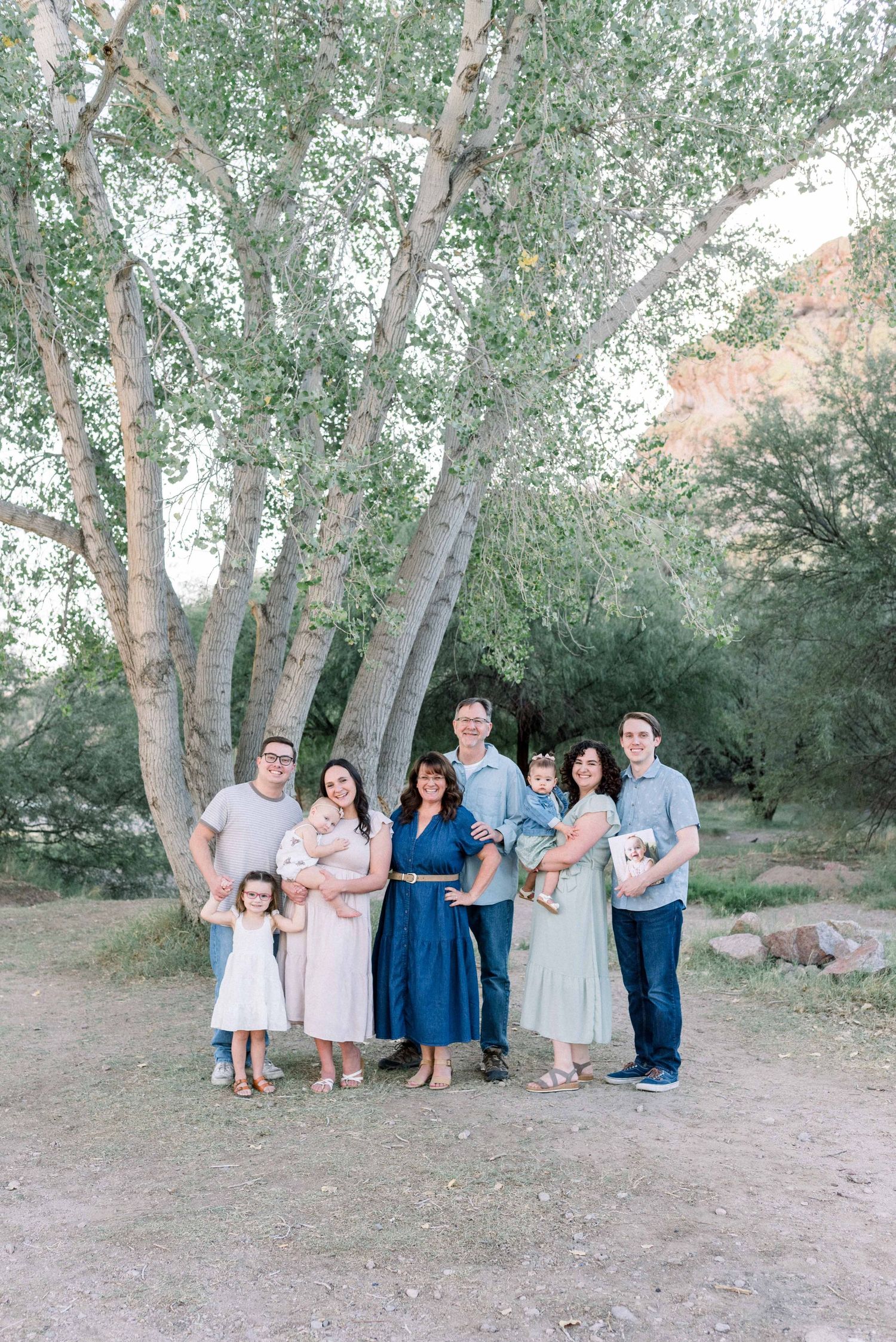 A group stands together under tall silver birch trees in a natural outdoor setting wearing coordinated blue and neutral tones.