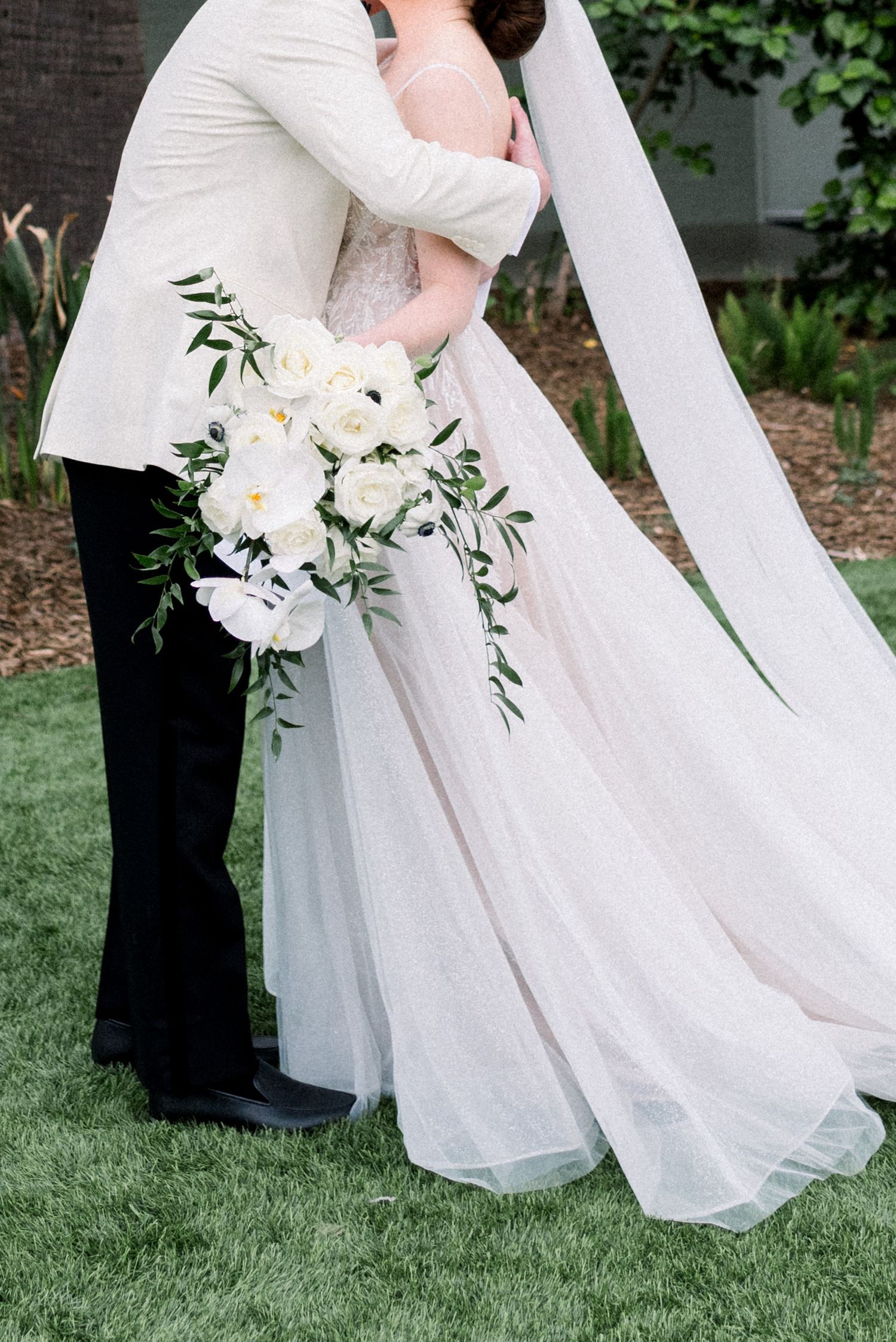 Elegant white wedding dress details with delicate floral accents against green grass.