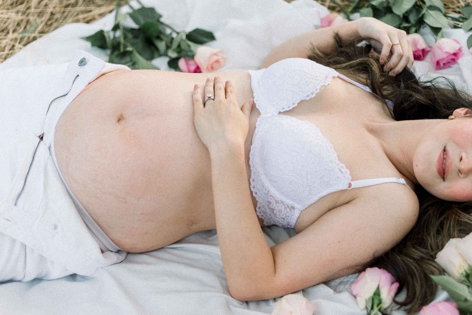 Intimate maternity photo with pink roses and white lace against natural backdrop.