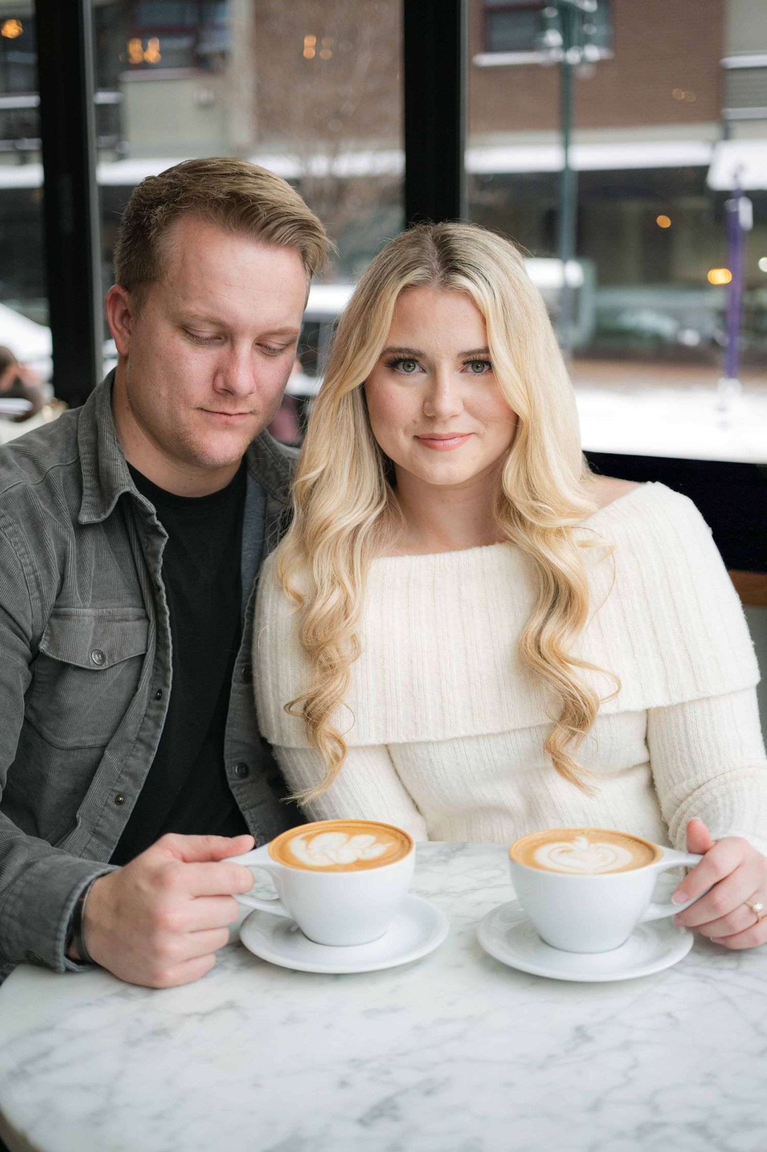 A couple poses together at a cafe table with matching cappuccinos.