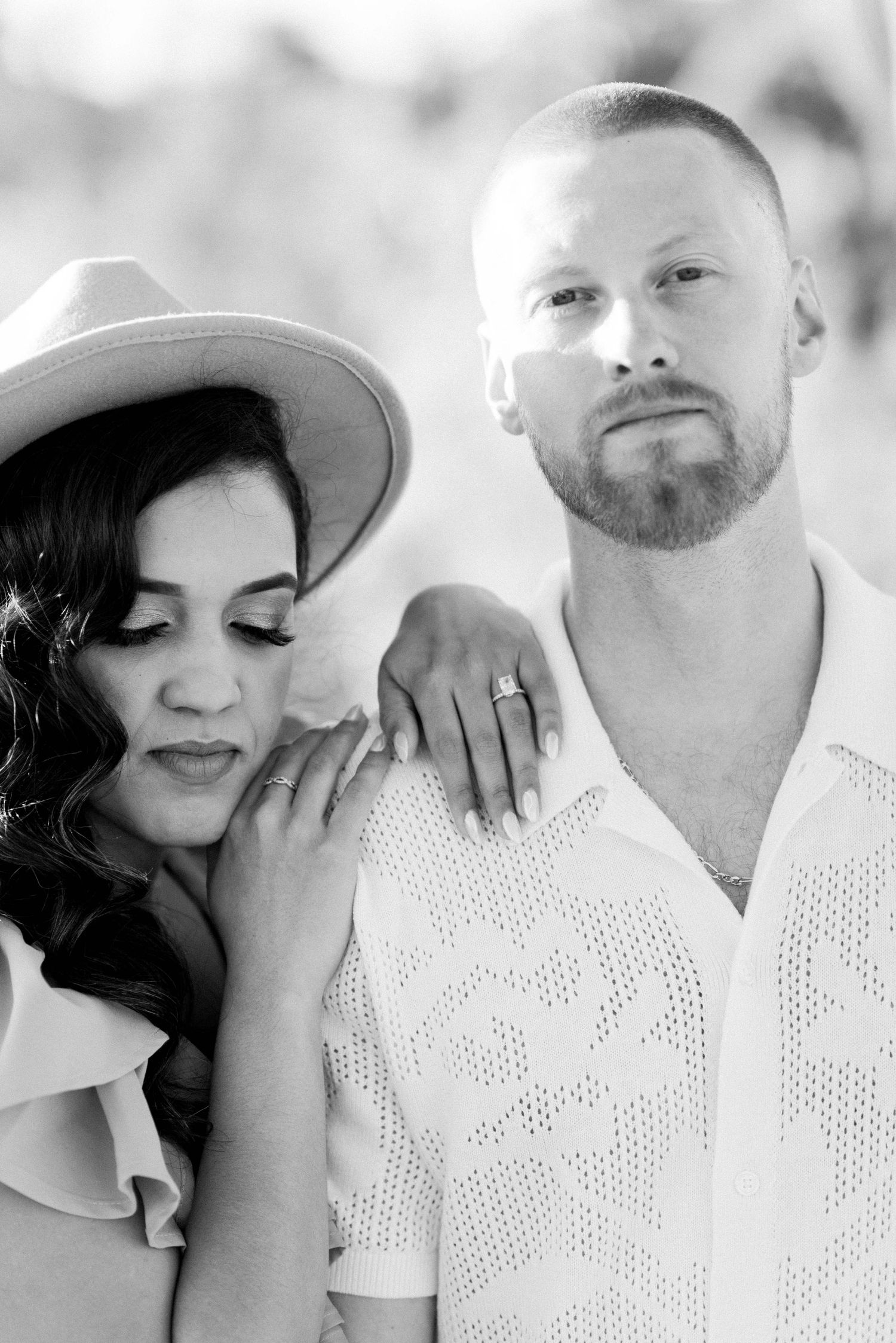 A black and white portrait of a couple with woman in hat leaning on man in white shirt.