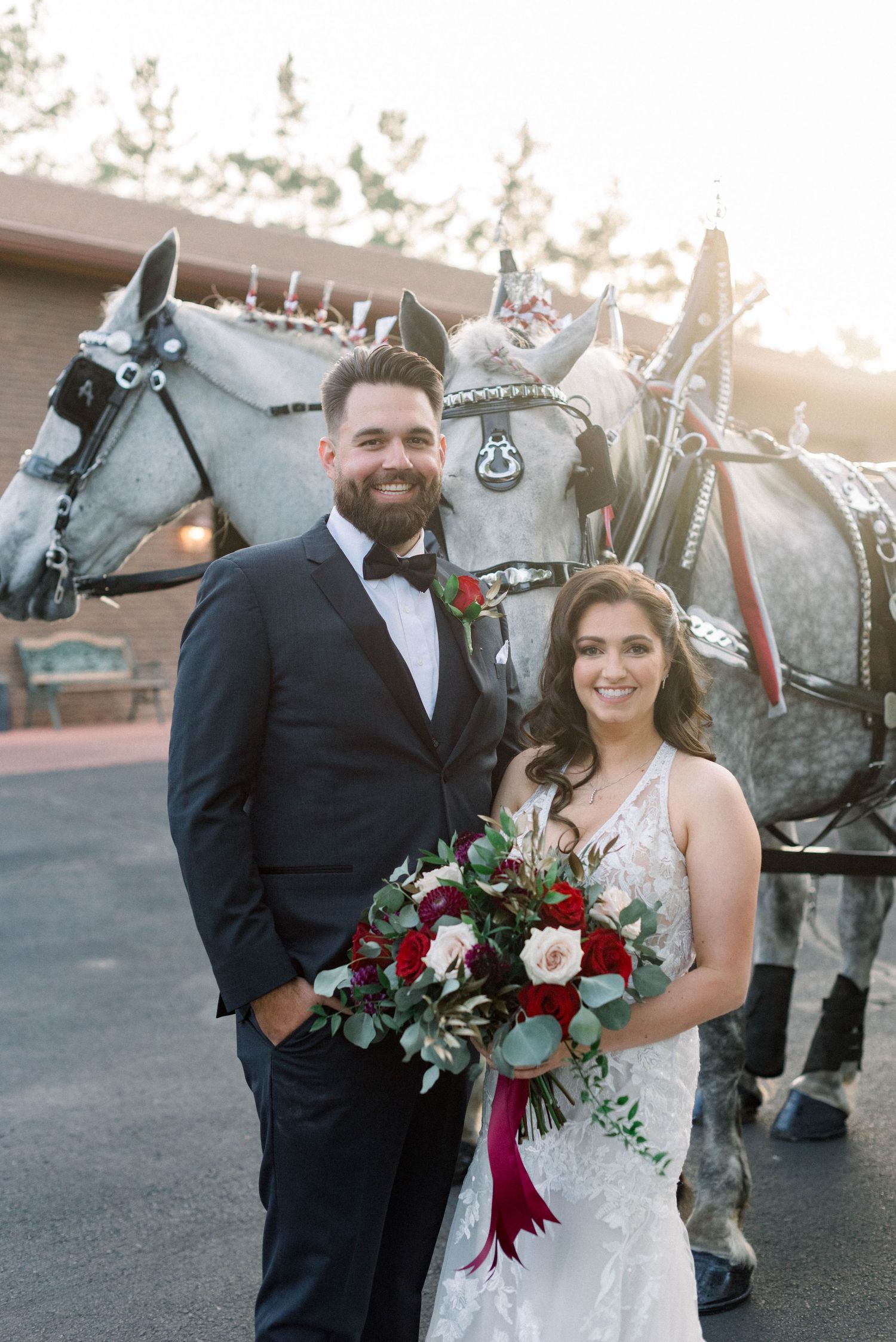 Couple poses with decorated white horses and carriage at sunset.