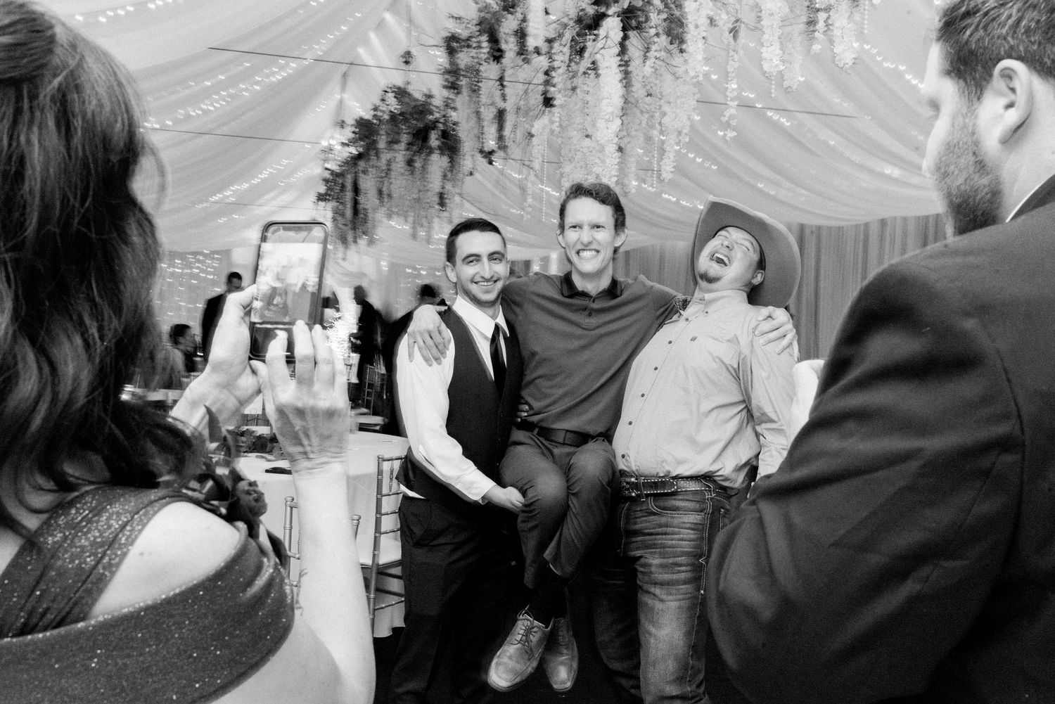 Black and white photo of guests laughing and celebrating at indoor wedding reception.