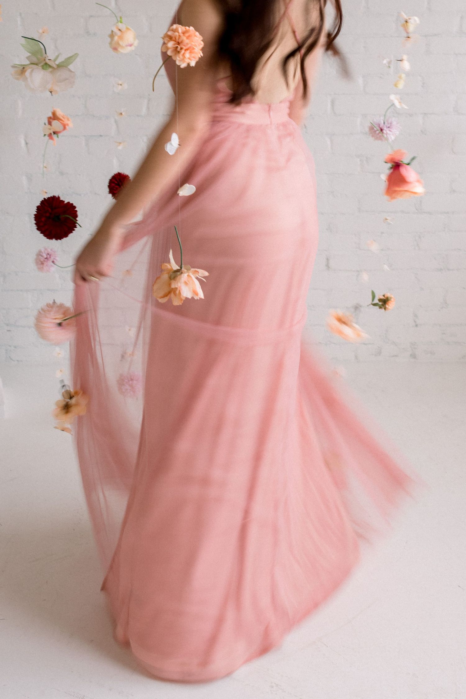 Twirling motion shot of pink dress with scattered flowers against white wall.