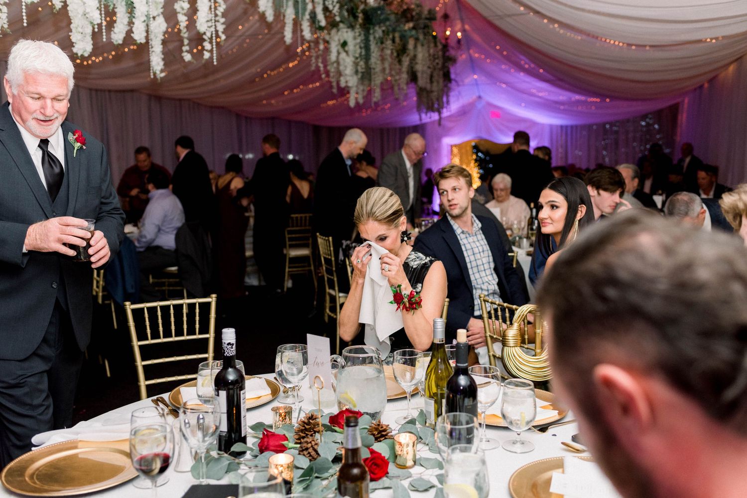Wedding reception dinner with guests seated at round tables under elegant draping and chandeliers.