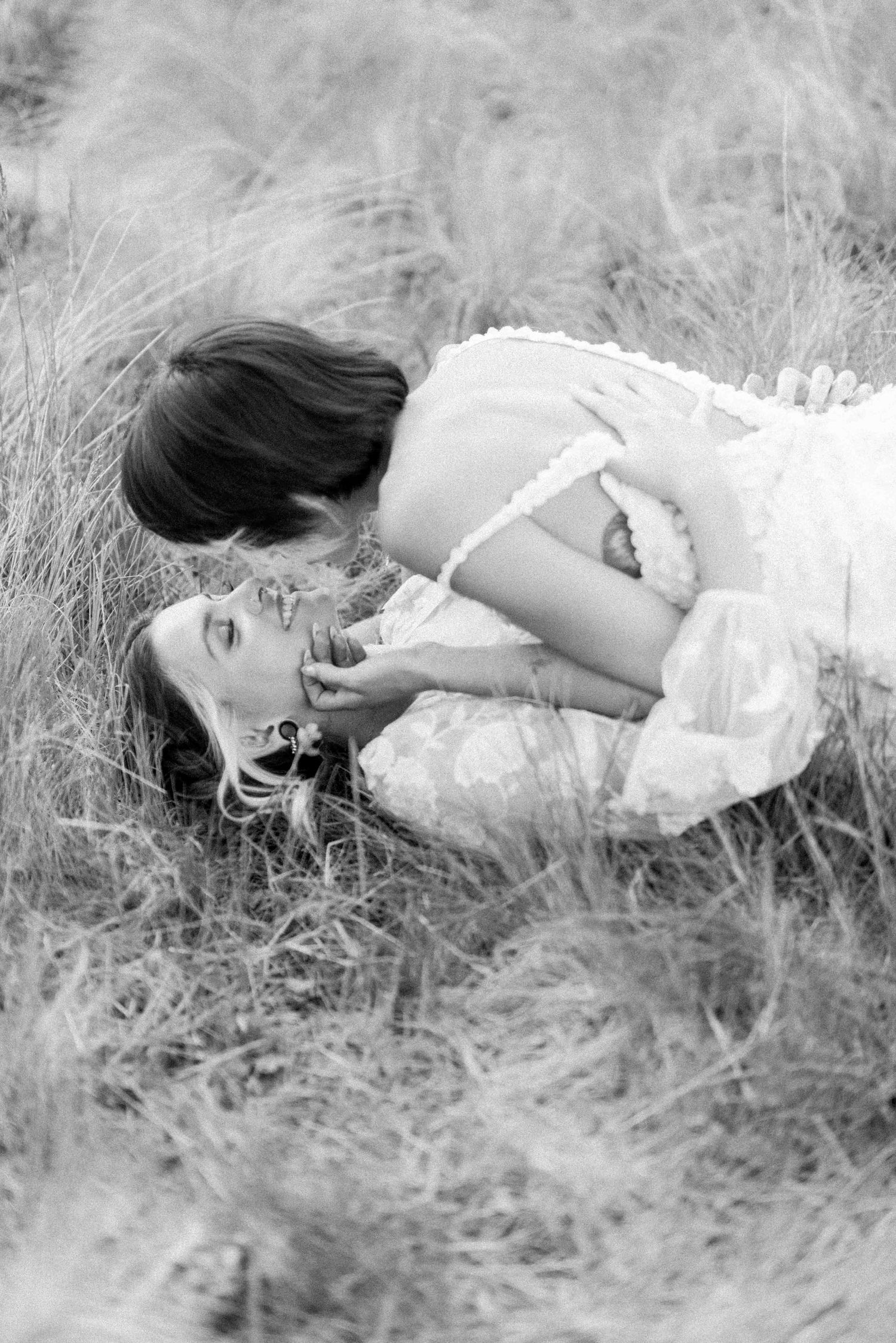 Romantic black and white photo of couple laying in meadow grass.