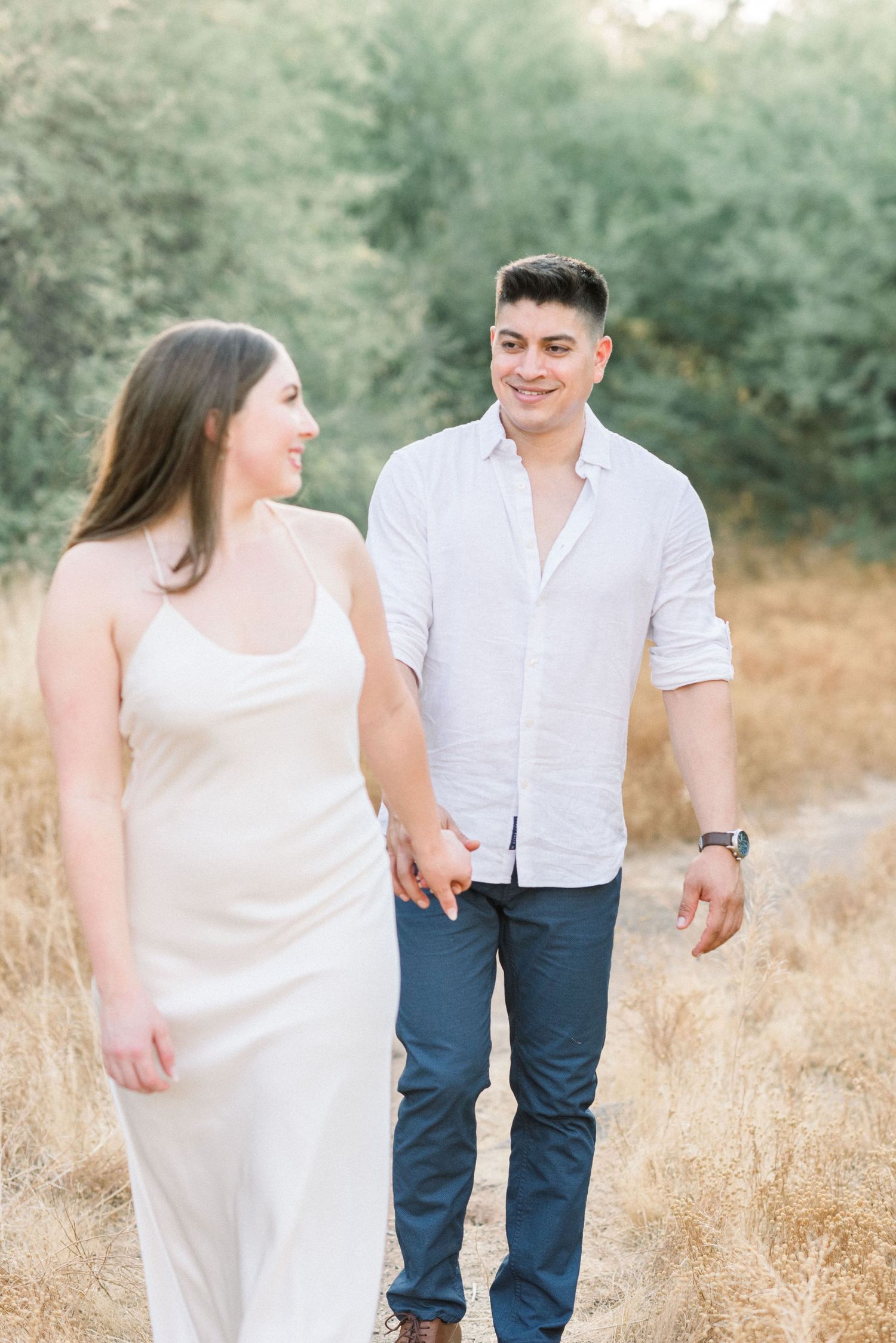 Couple walking together through a sunlit golden field on a summer afternoon.