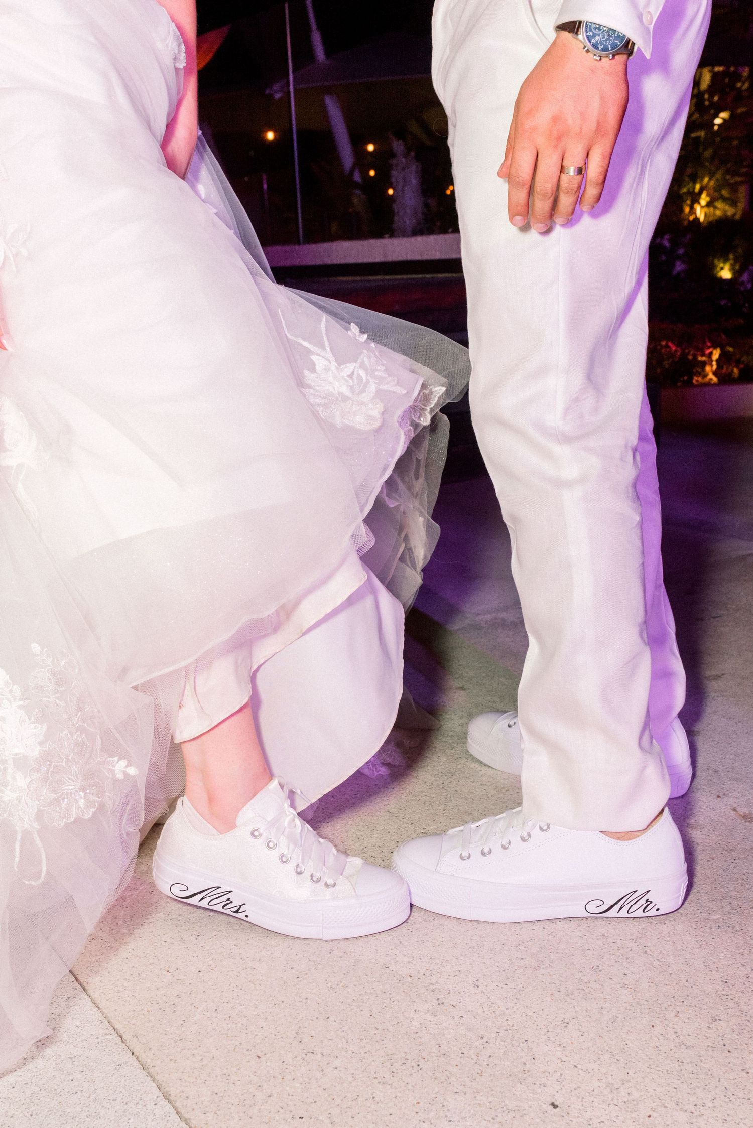 Close-up of bride and groom's matching white wedding sneakers on dance floor.