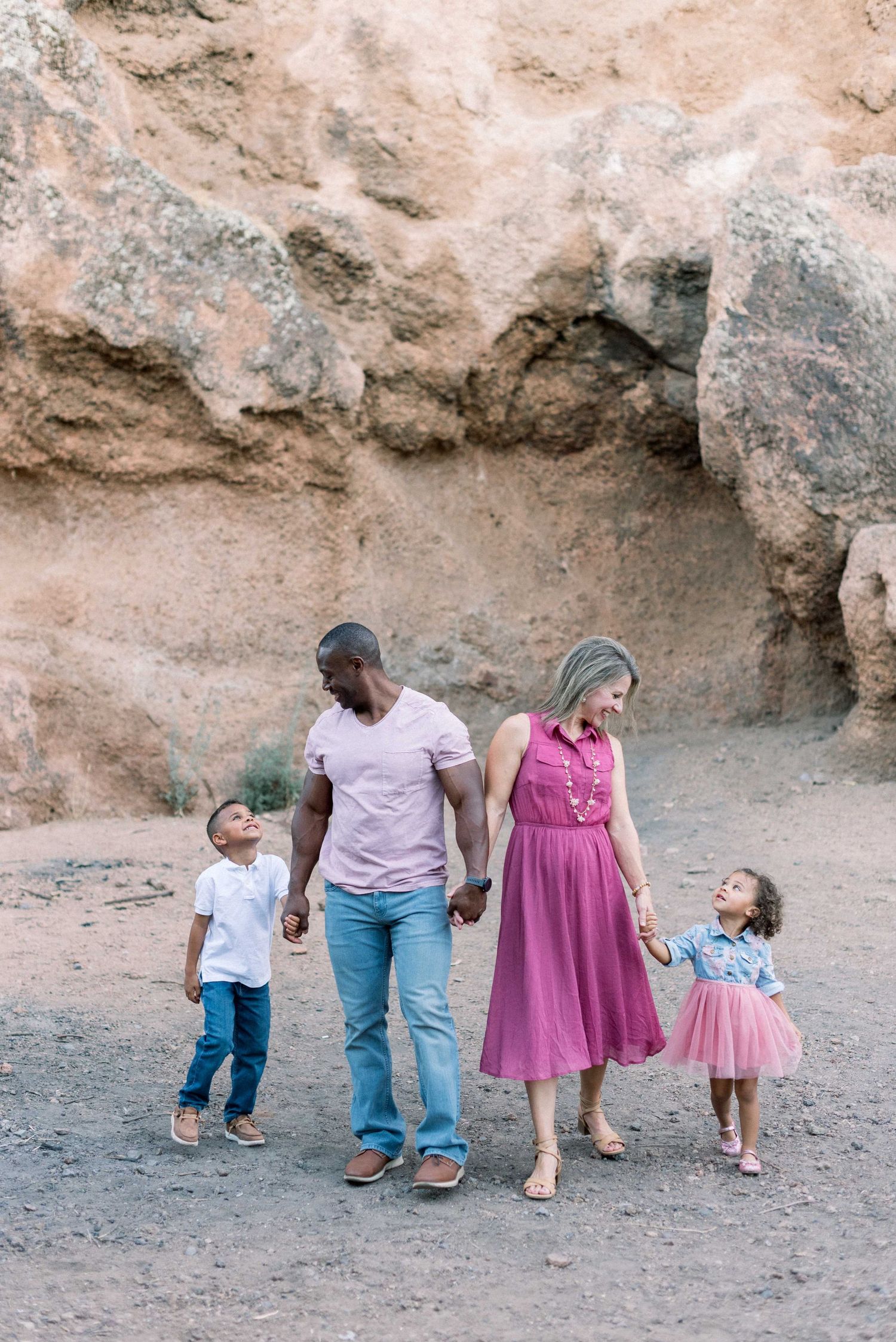 A family walks together along a rocky desert path wearing coordinated outfits in pink and blue tones.