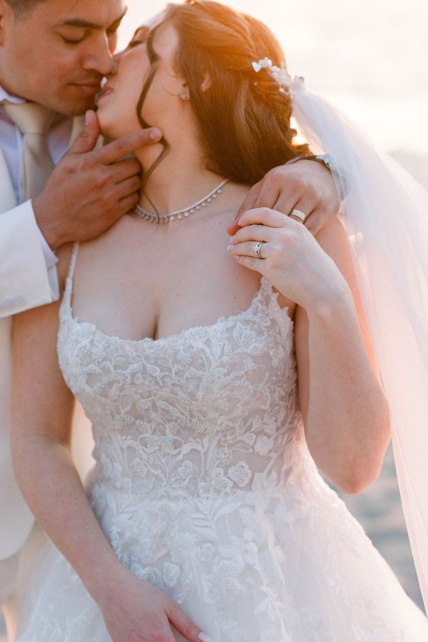 An intimate wedding portrait showing delicate lace details and jewelry against a sunset beach backdrop.