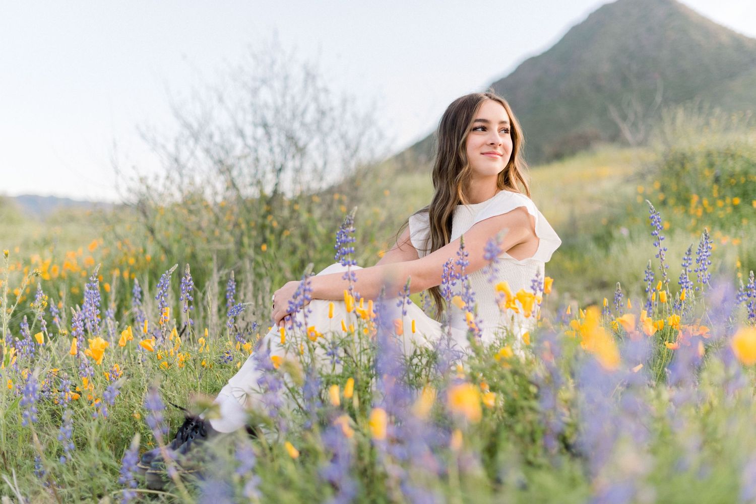 A portrait in a wildflower meadow with purple lupines and yellow blooms against hills.