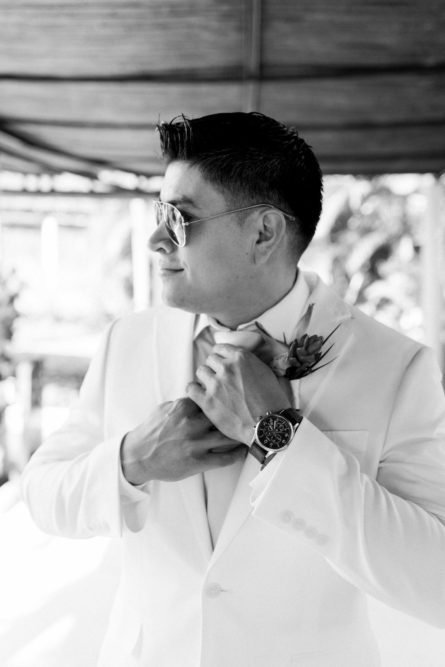 Black and white portrait of groom adjusting tie with boutonniere.