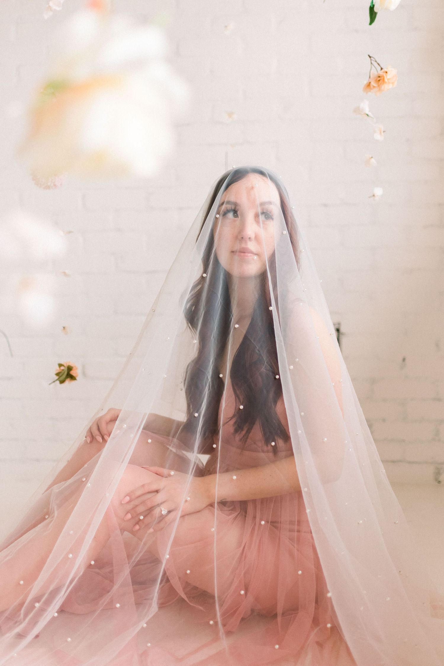 Dreamy veil-draped figure in pink dress surrounded by floating blooms.