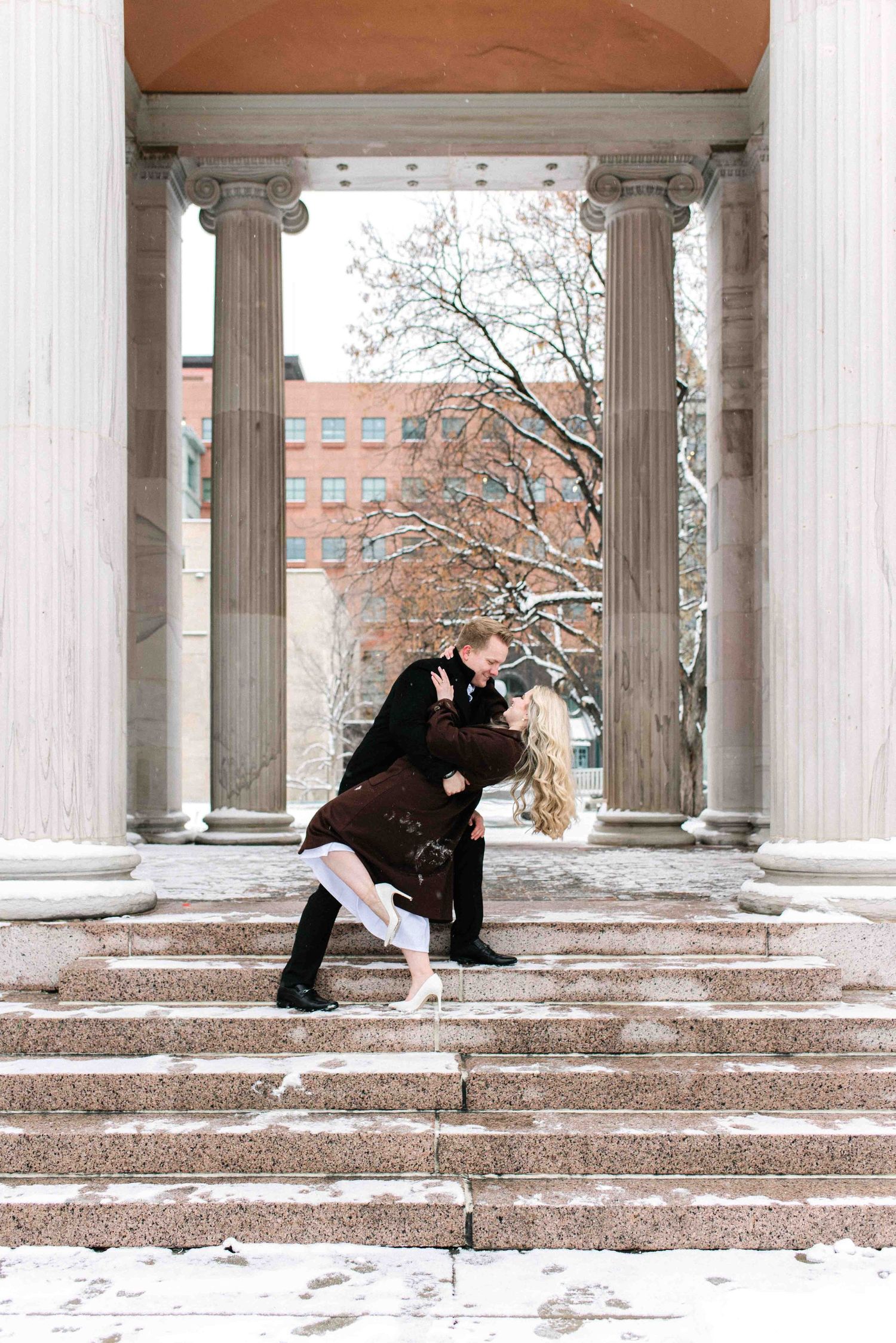 A romantic dip pose between classical columns on snowy steps.