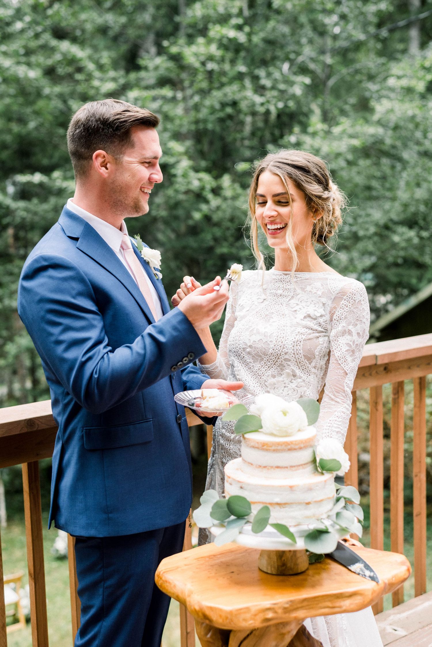 Couple shares a joyful moment while cutting their wedding cake on rustic wooden table.