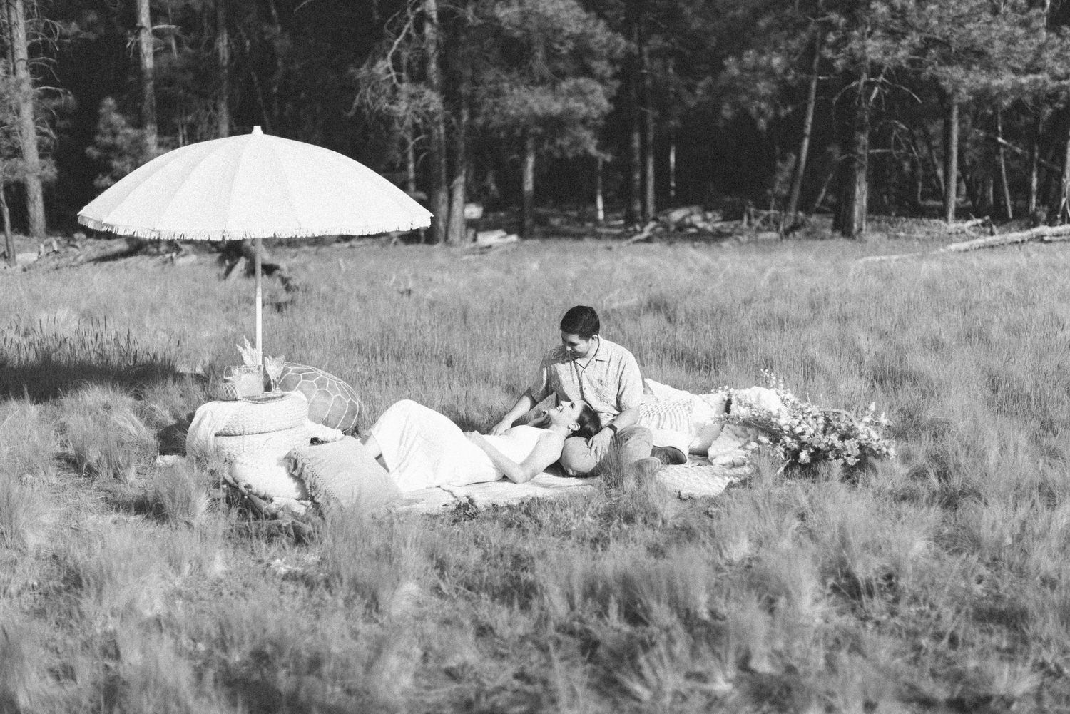 Black and white photo of romantic picnic scene with umbrella in open field.