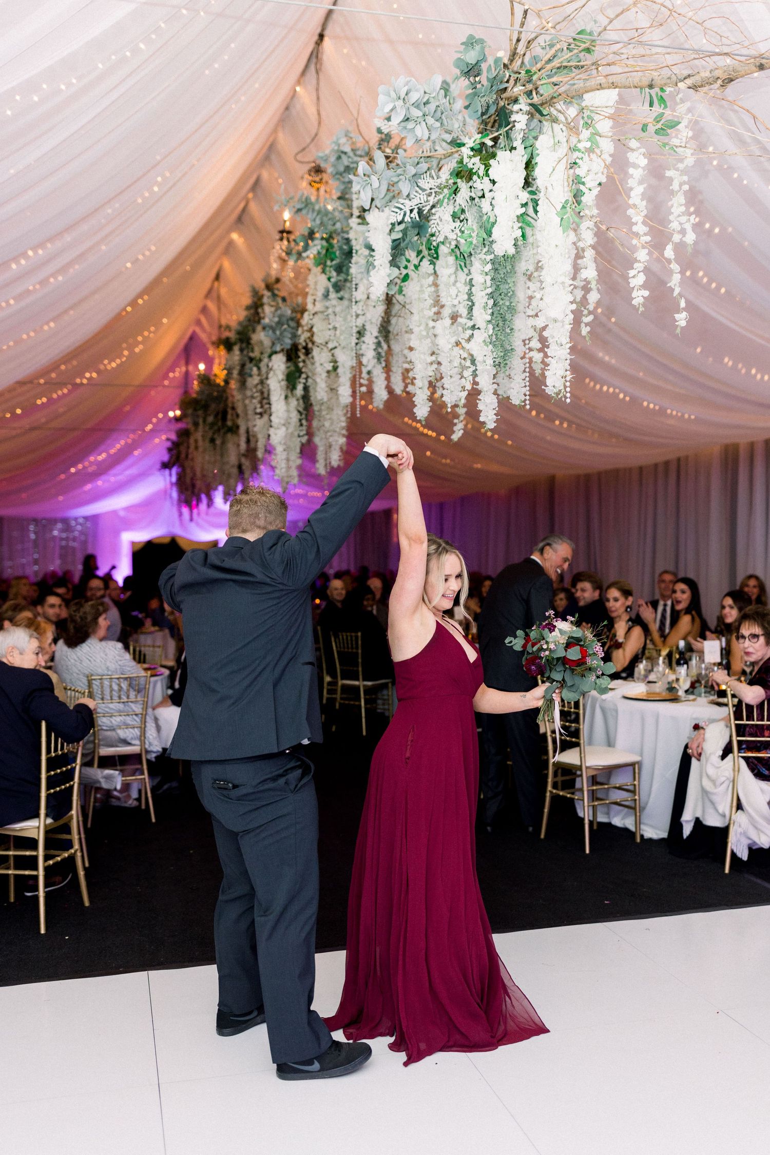 Couple dancing under elegant hanging floral arrangements at wedding reception.