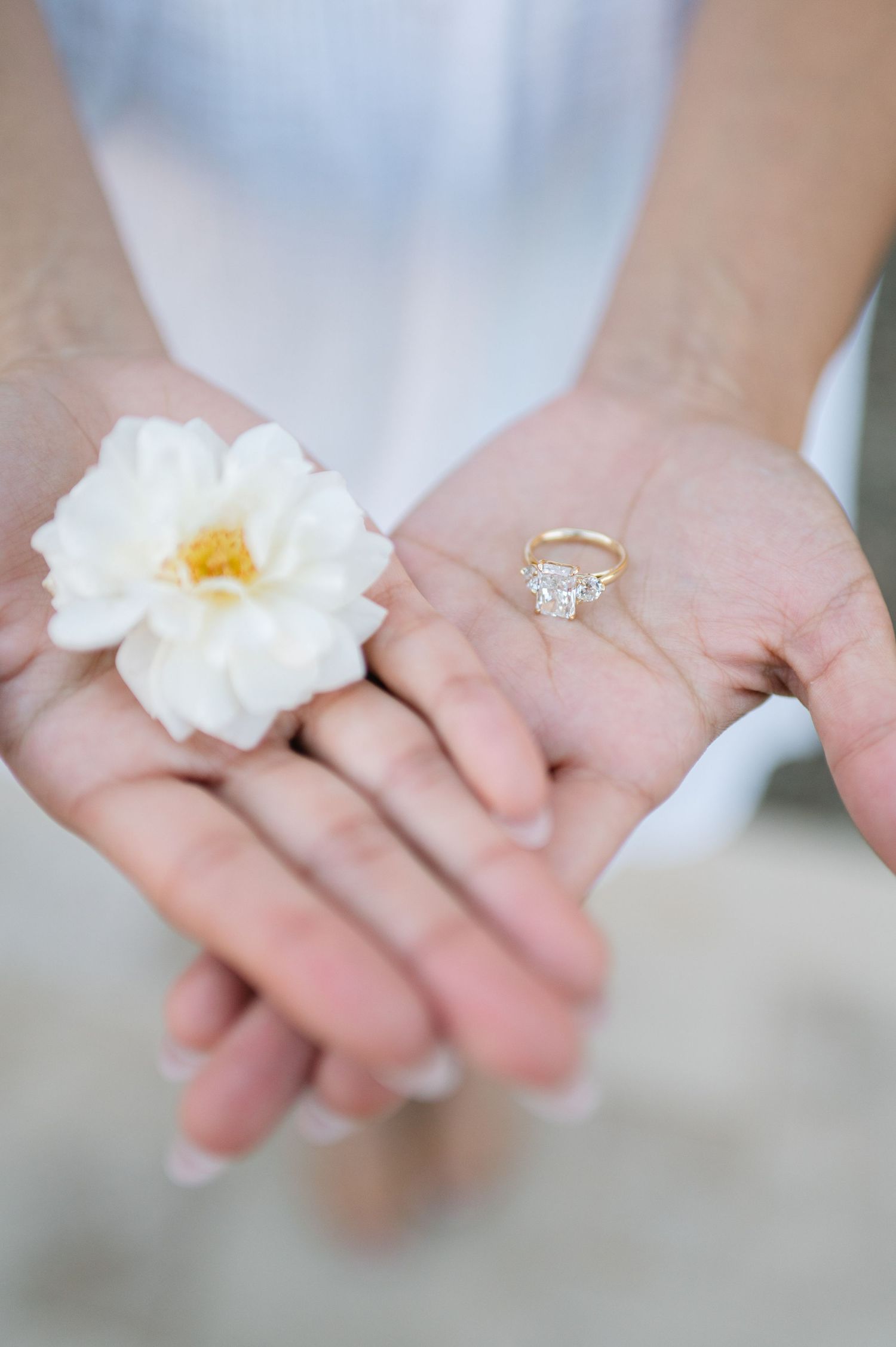 Close-up of hands wearing engagement rings with white flower.