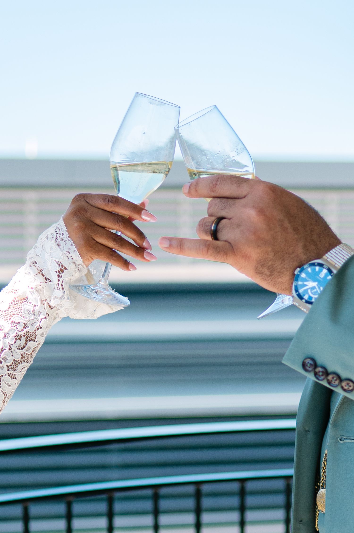 Two hands toasting with champagne glasses, one wearing lace sleeve and one with blue blazer and watch.