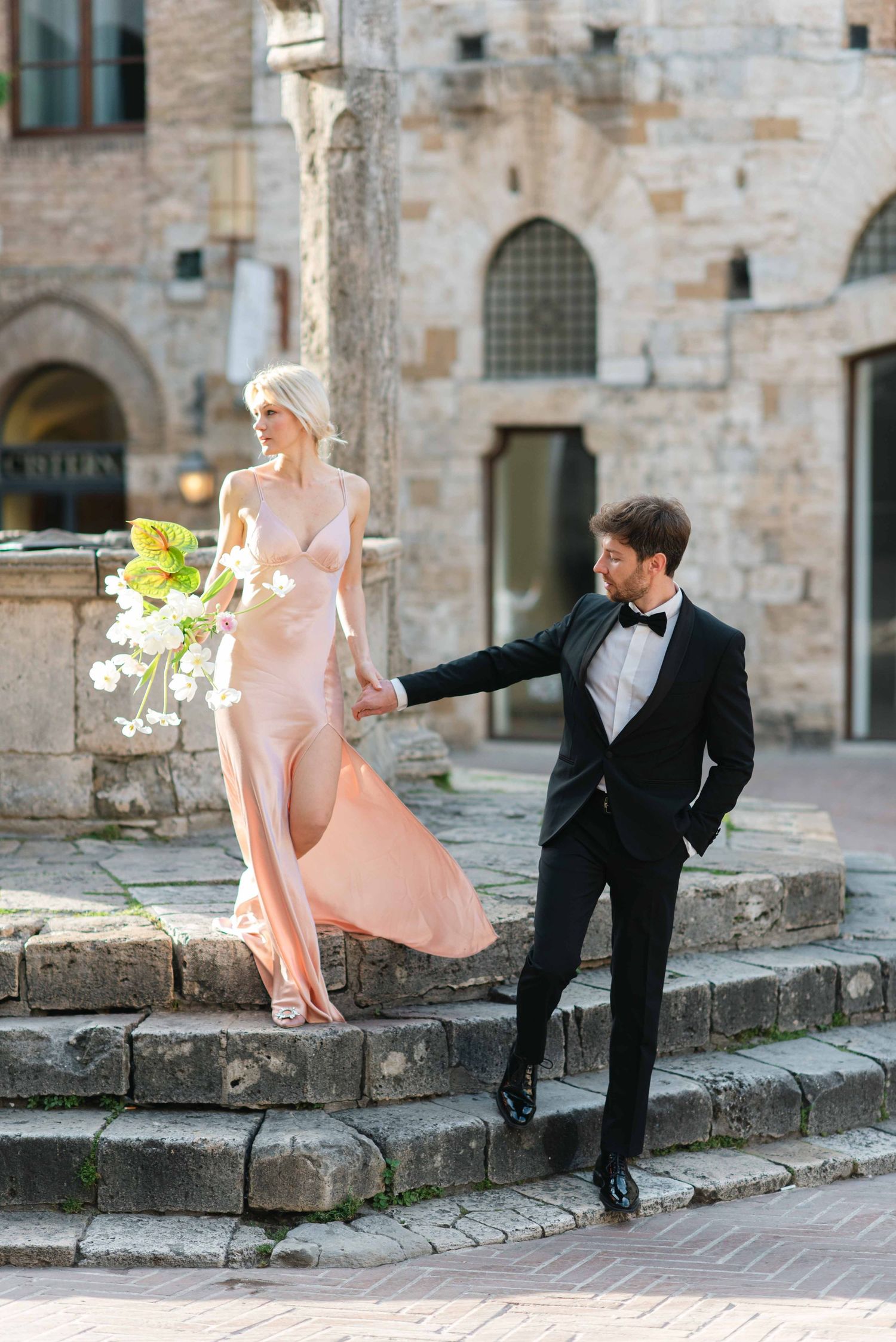Couple in formal attire sitting on stone steps of historic building.
