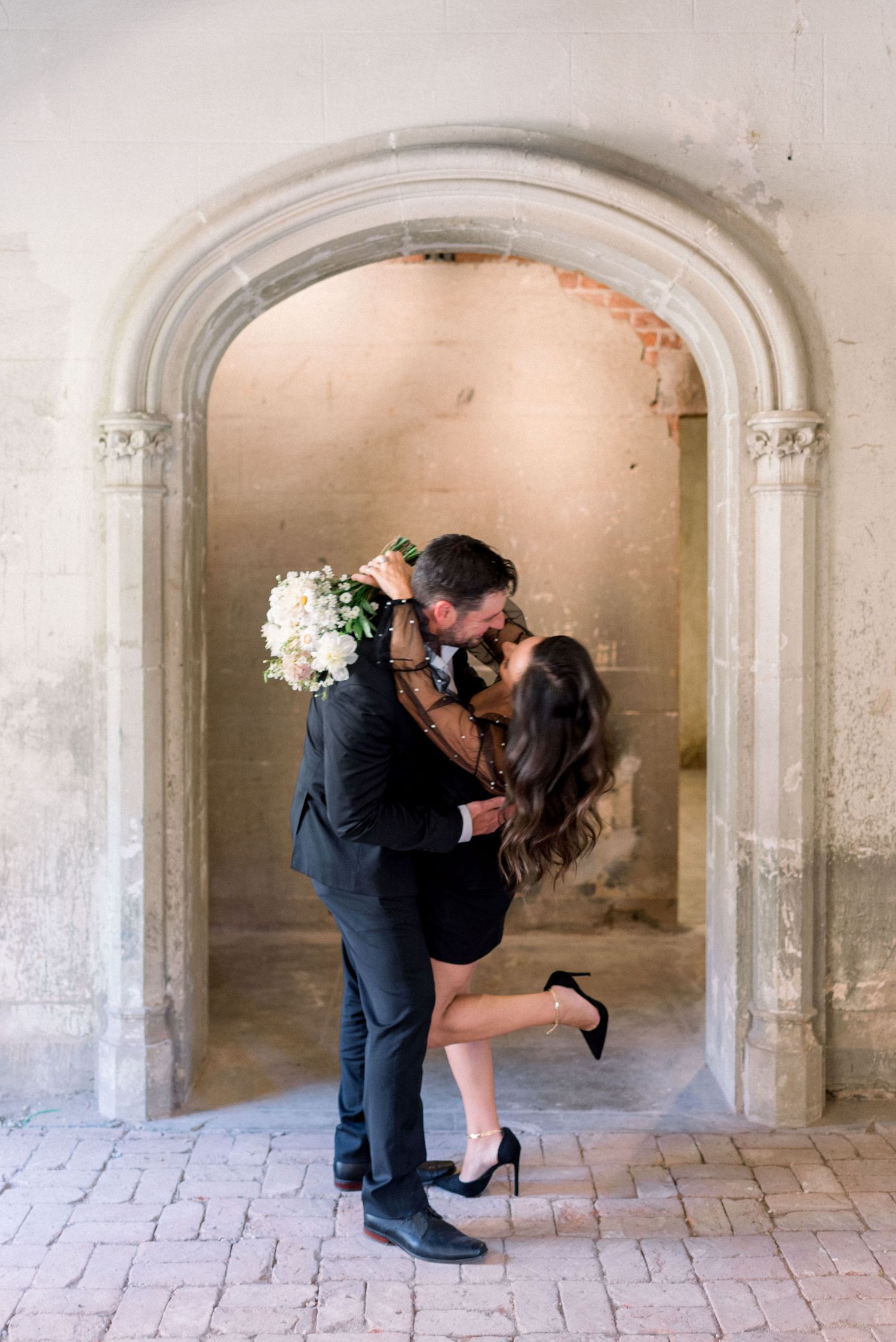 Romantic moment captured in an arched stone doorway with a bouquet.