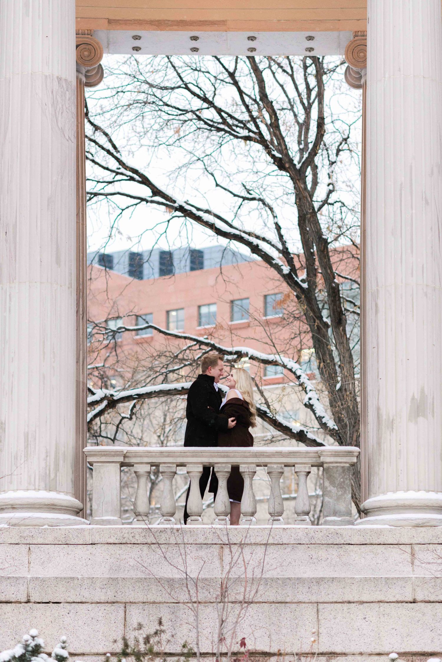 Silhouette of a couple embracing between classical columns with snow-covered trees.