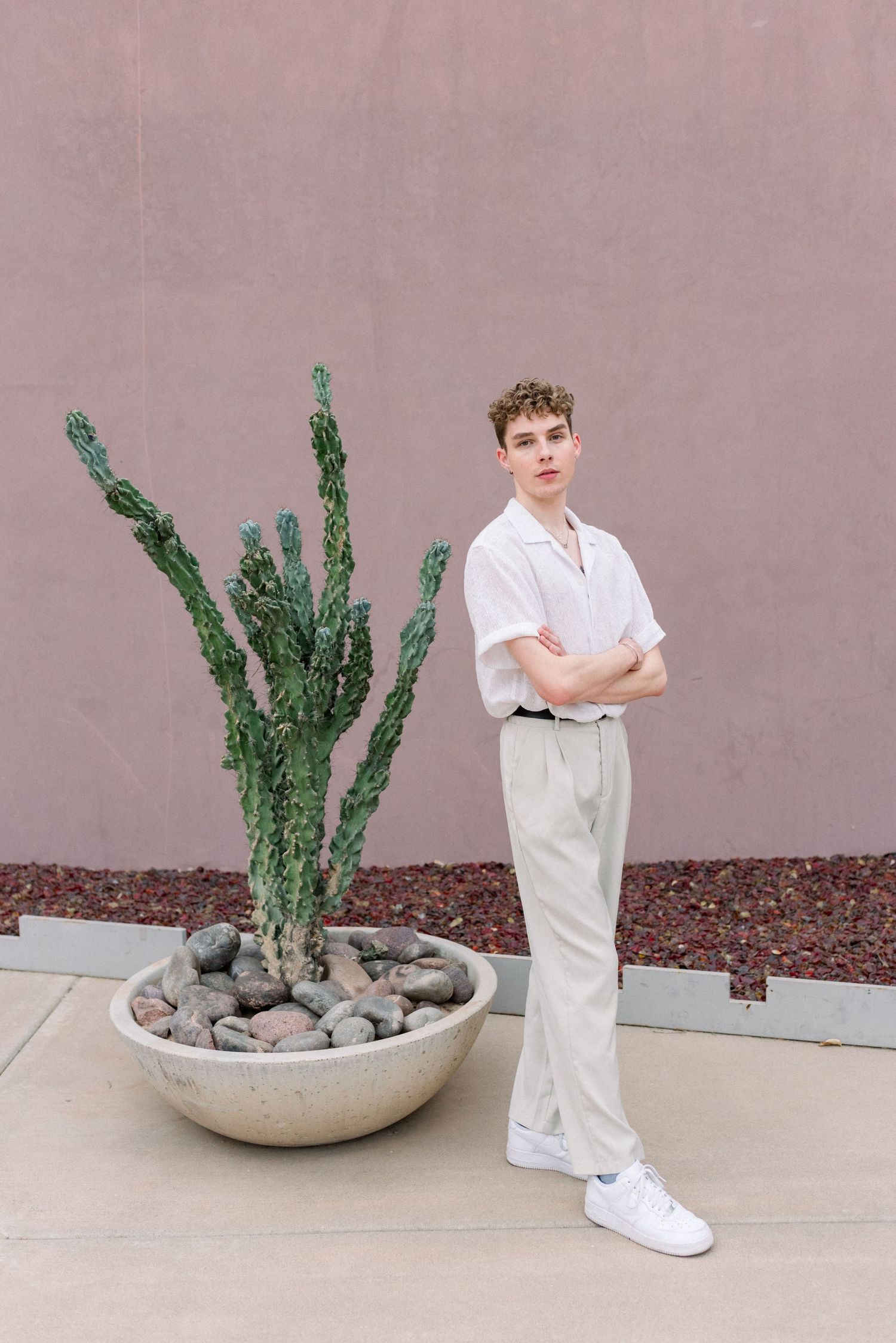 Modern minimalist fashion portrait with white shirt and khaki pants beside desert plant.