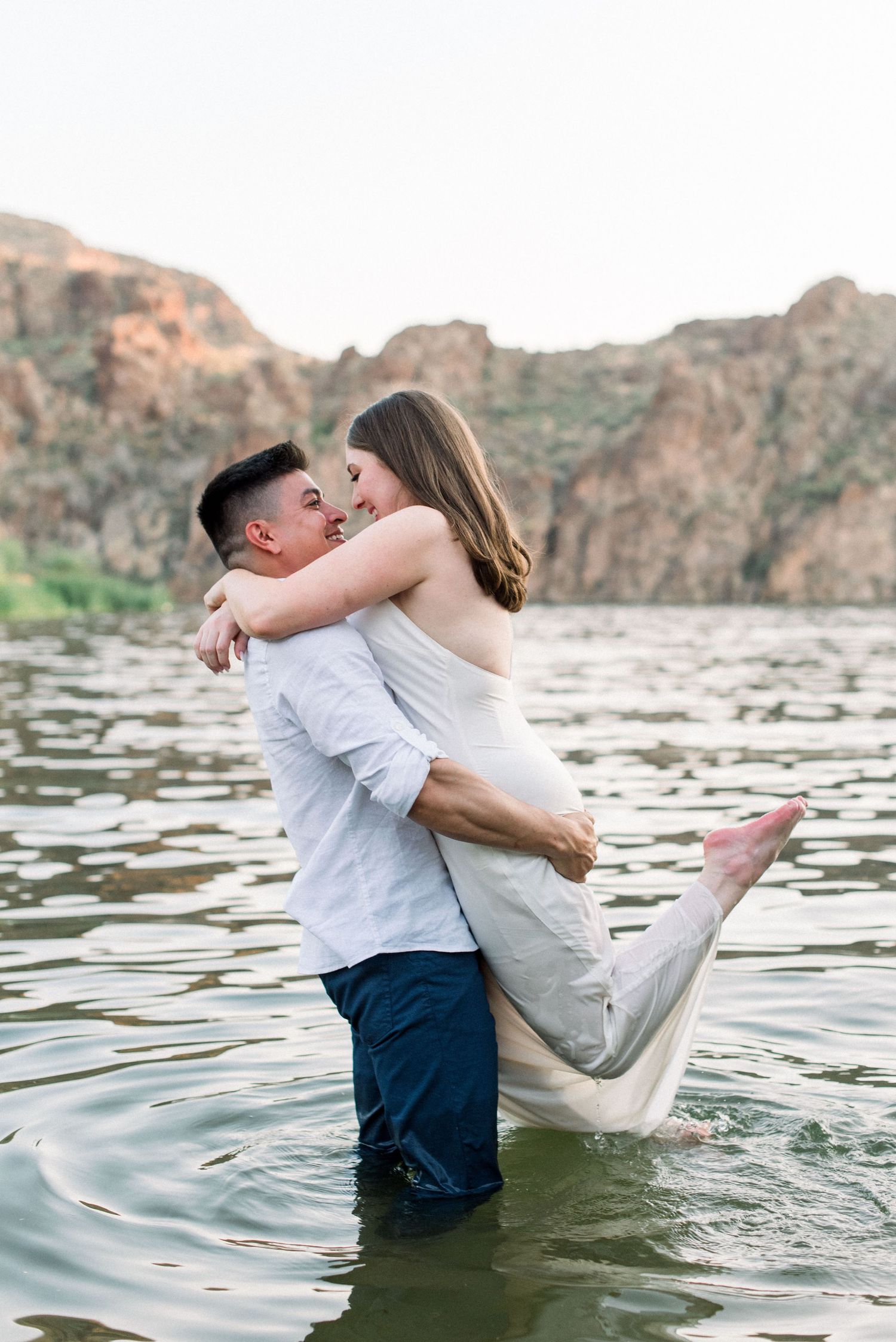 Romantic couple embrace while standing in water with scenic canyon backdrop.