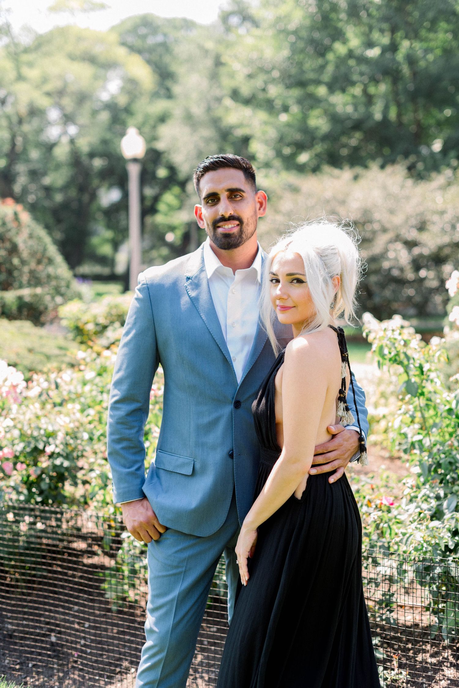 Couple in blue suit and black dress posing in a blooming garden.