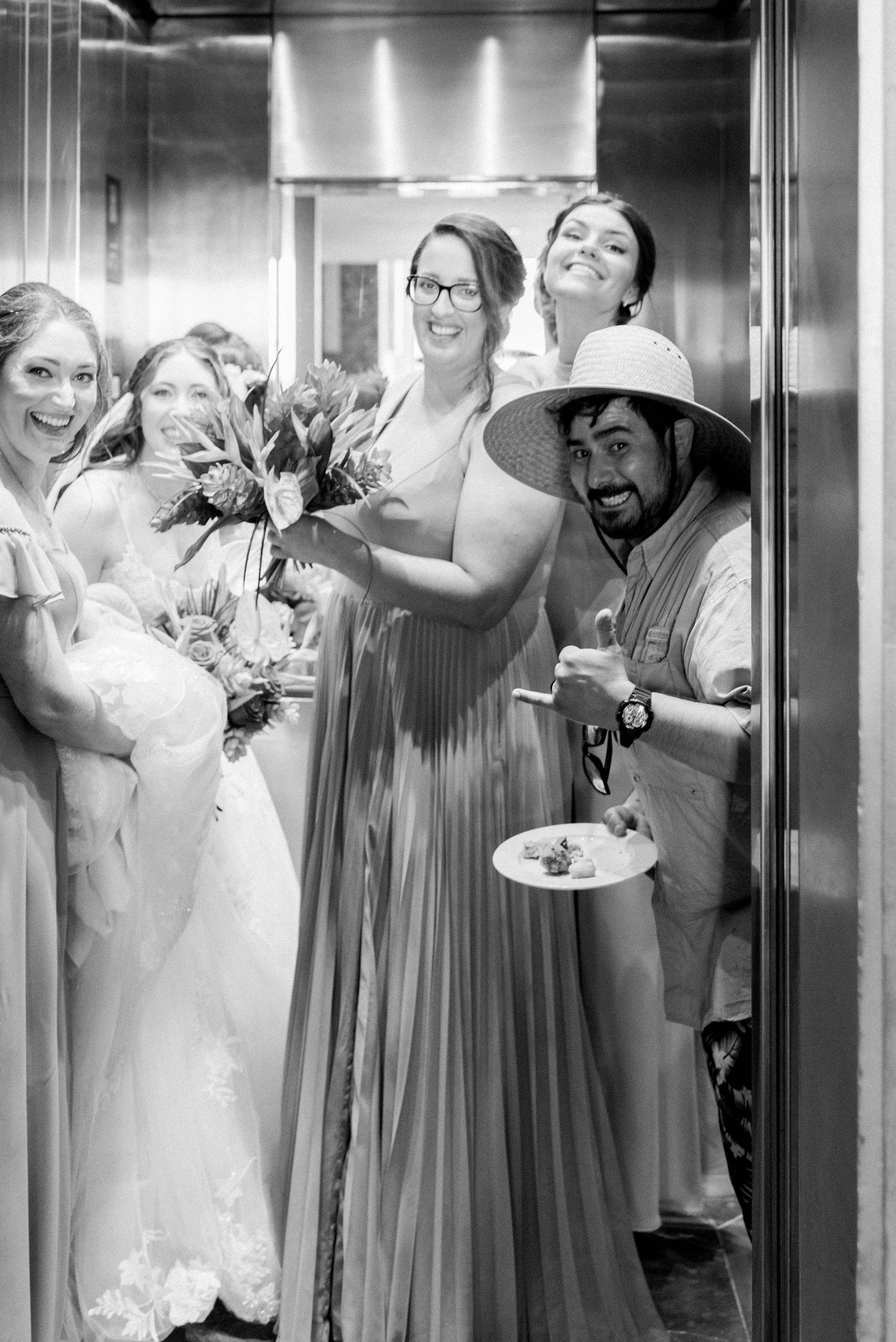 Wedding party sharing joyful laughter while crowded in an elevator with bouquets and champagne.