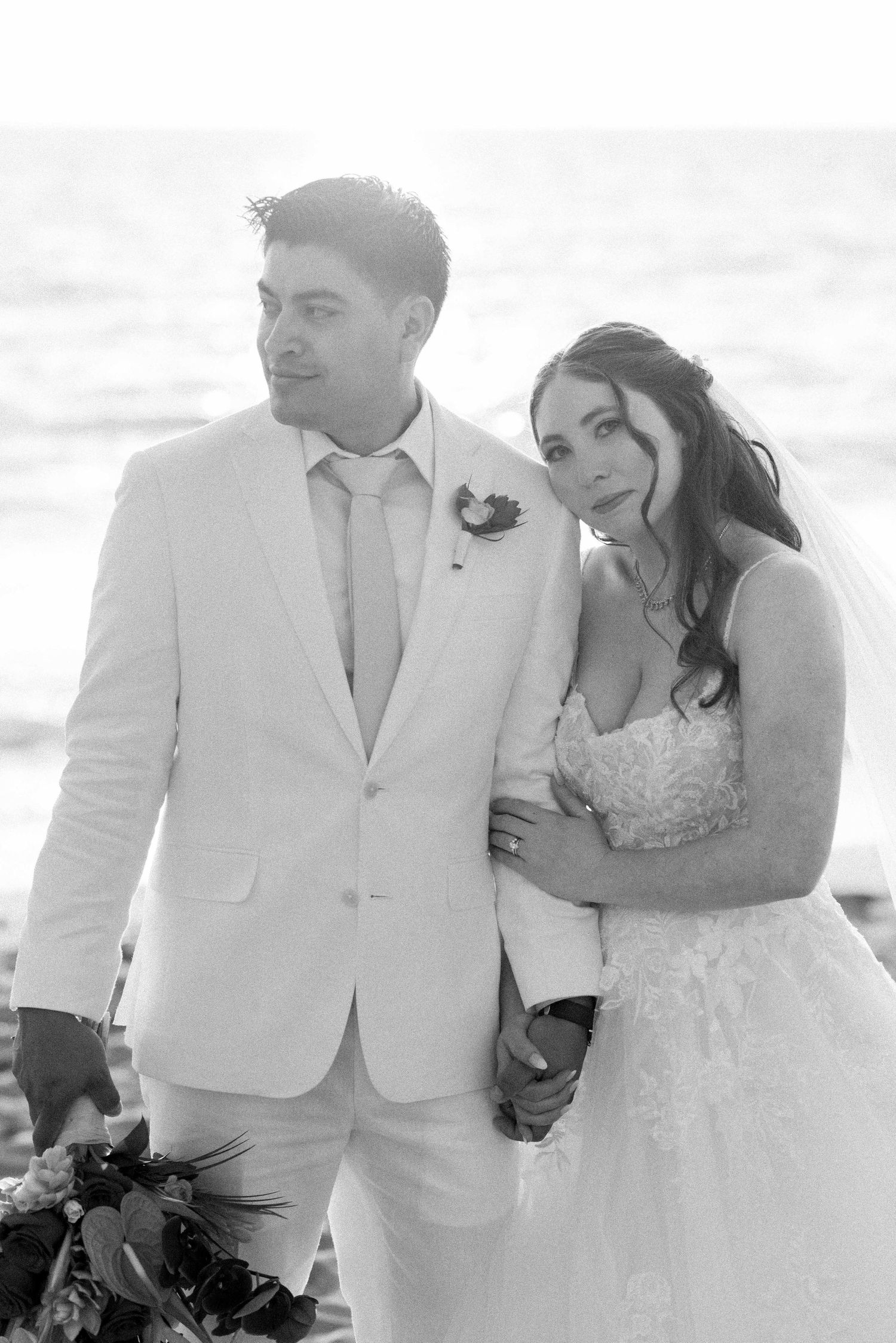 Black and white beach wedding portrait with couple in white attire and tropical bouquet.
