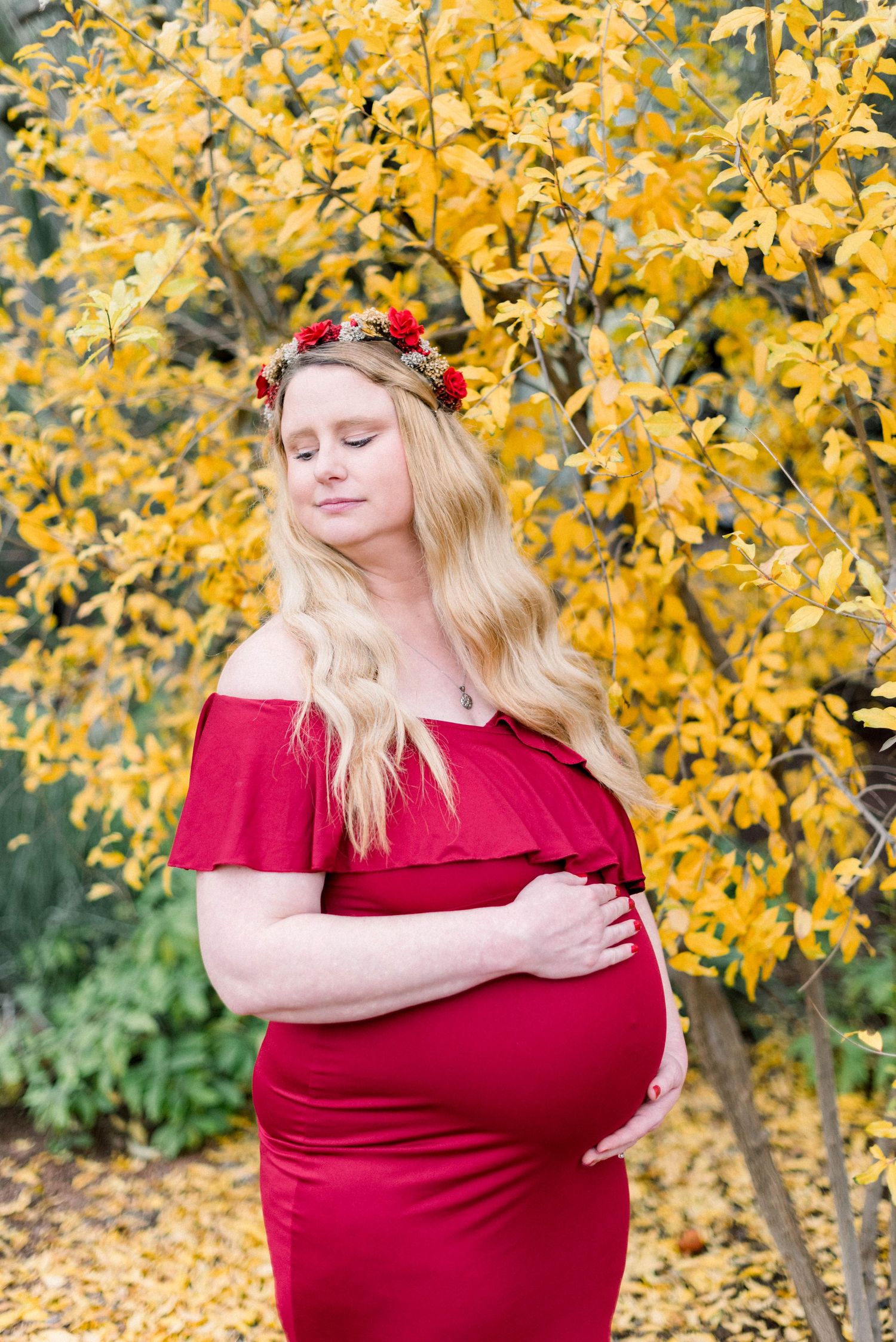 Maternity photo in red off-shoulder dress against vibrant yellow autumn foliage.