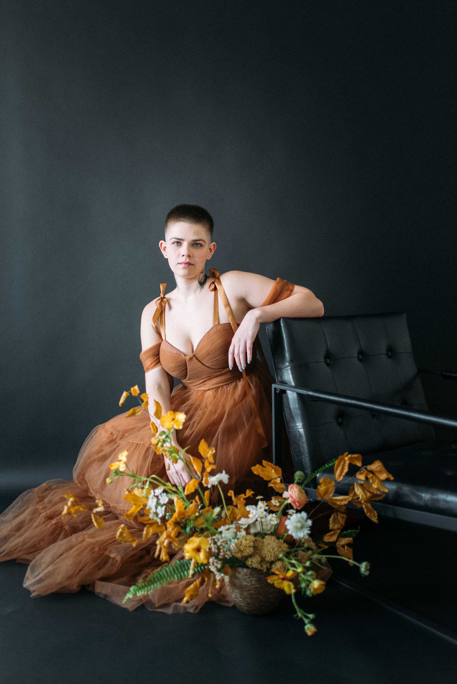 Someone poses elegantly by a black leather bench with yellow florals in a brown formal gown.