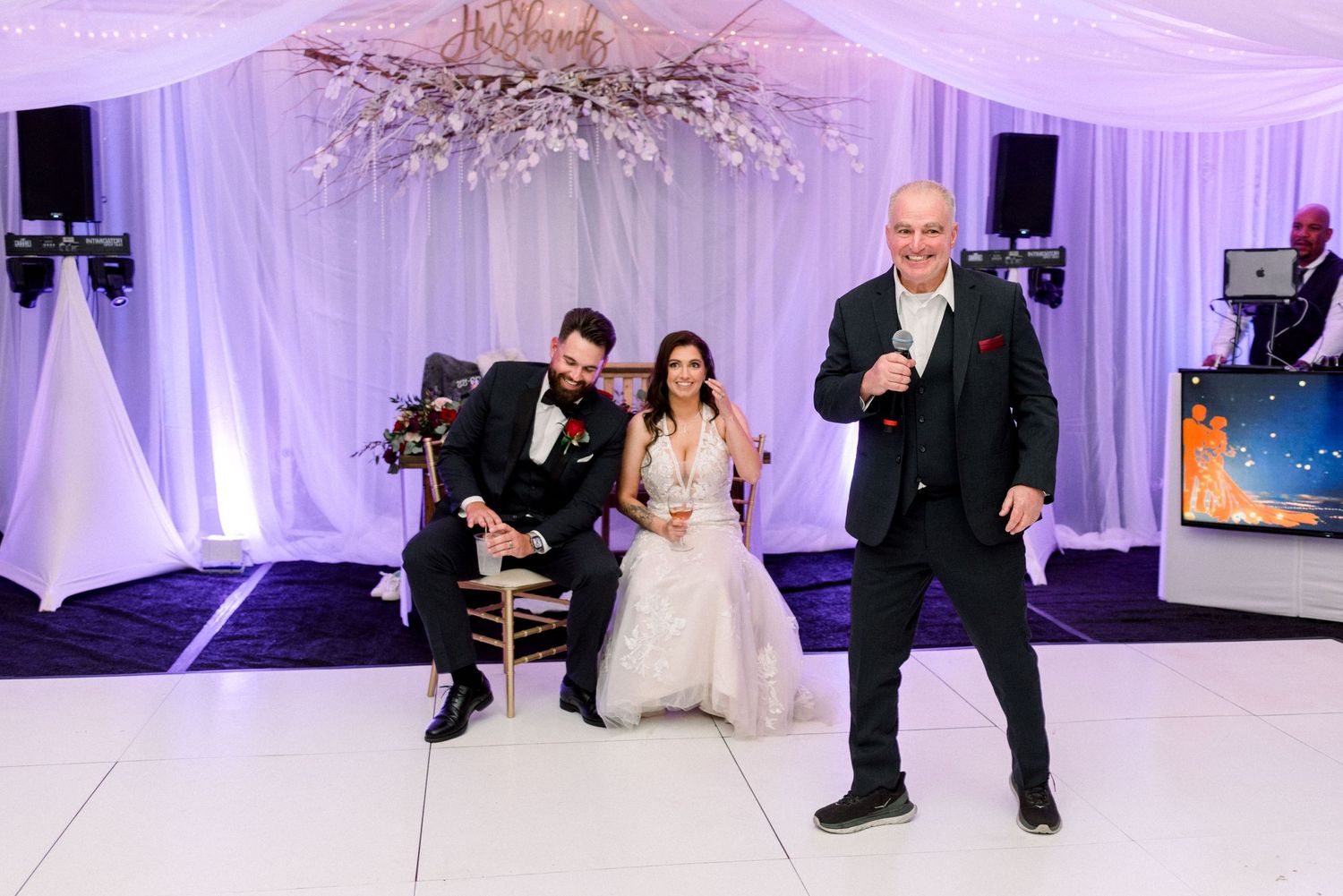 Wedding celebration in a purple-lit tent venue with guests enjoying entertainment and festivities.