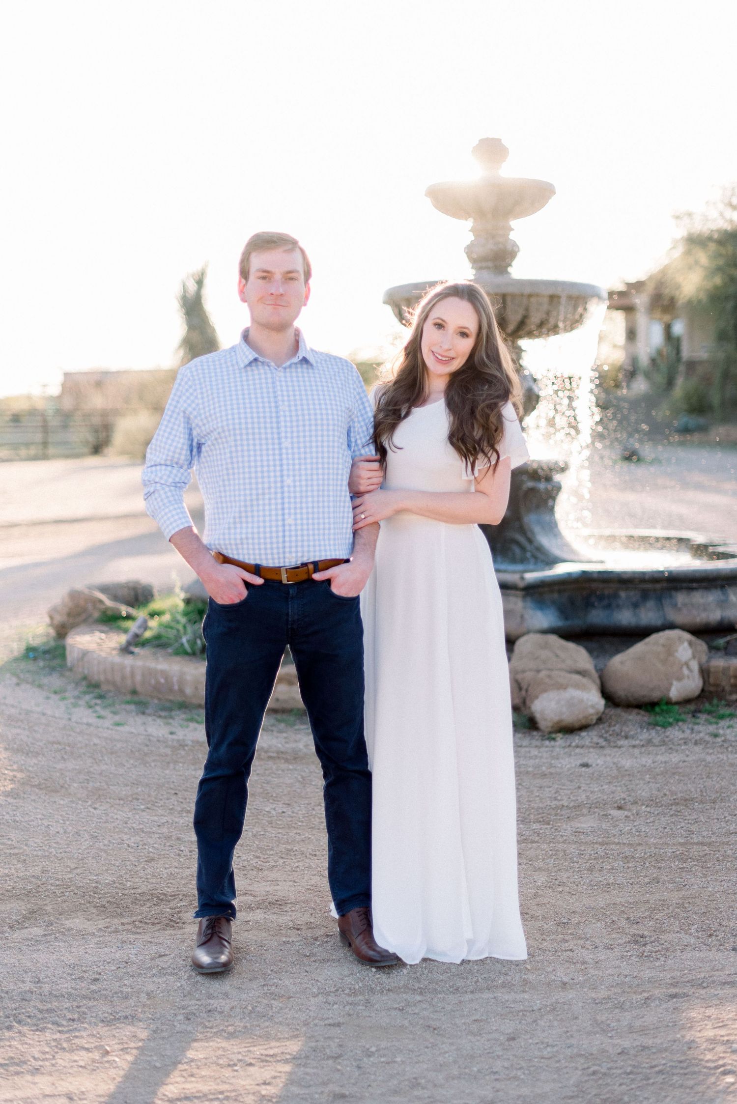 Desert engagement photo with fountain backdrop and coordinated blue and white outfits.