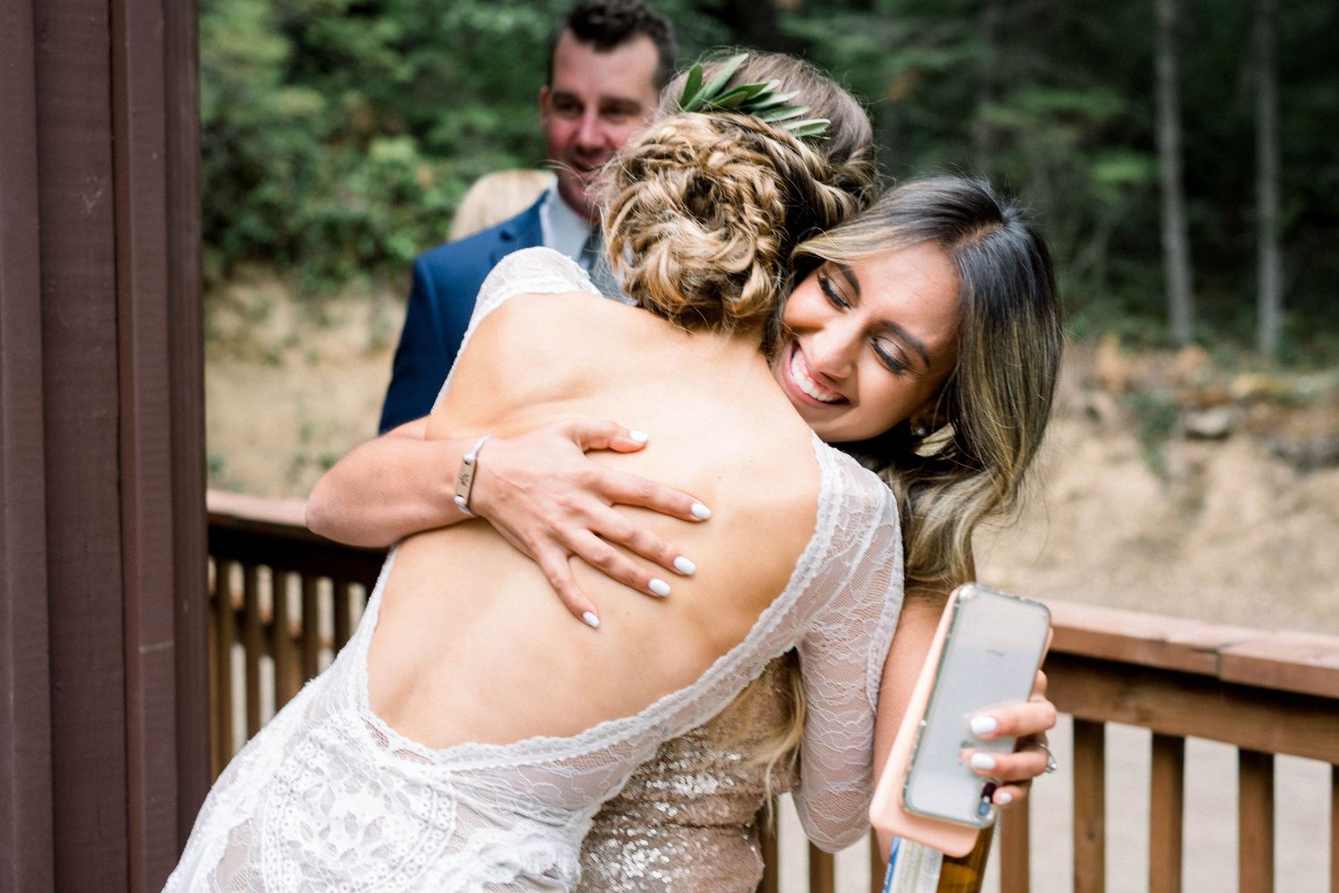 A warm embrace shared between guests at an outdoor wedding ceremony on a wooden deck.