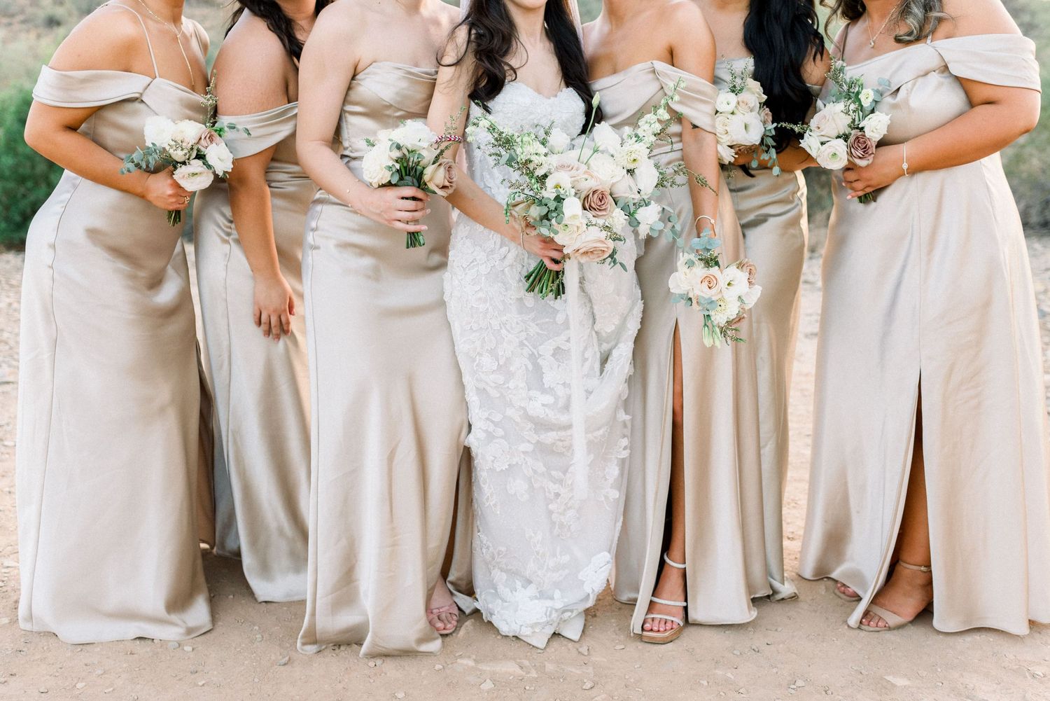 Bridesmaids in champagne-colored dresses holding white floral bouquets.