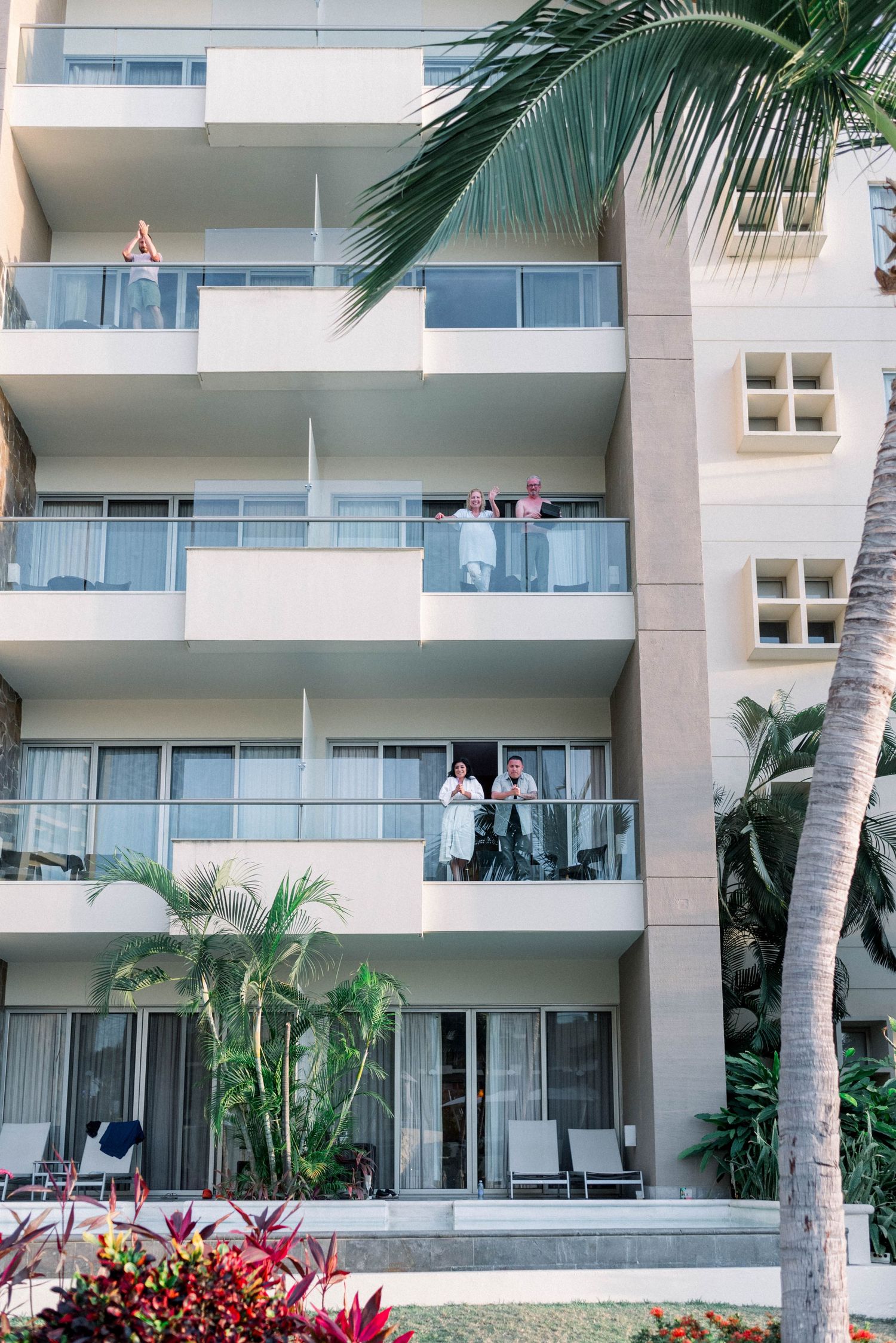 Modern white apartment building with palm trees and balconies in a tropical setting.