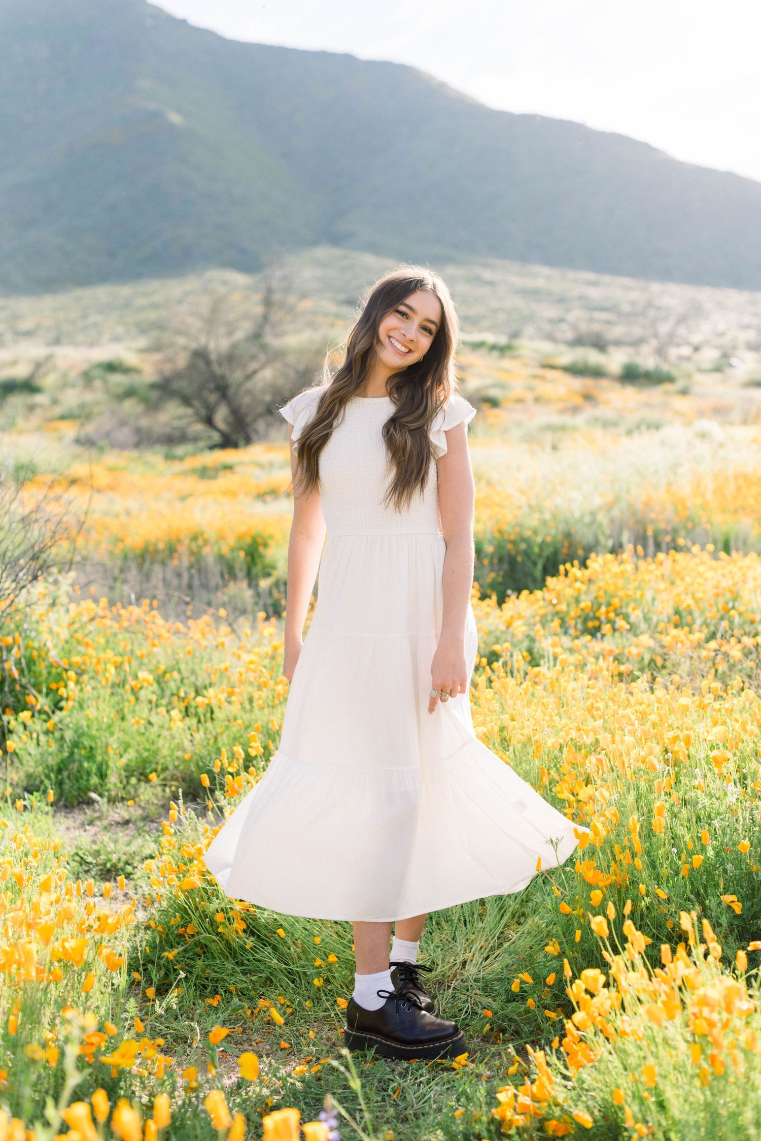 White dress twirling in a field of yellow flowers with mountains in background.