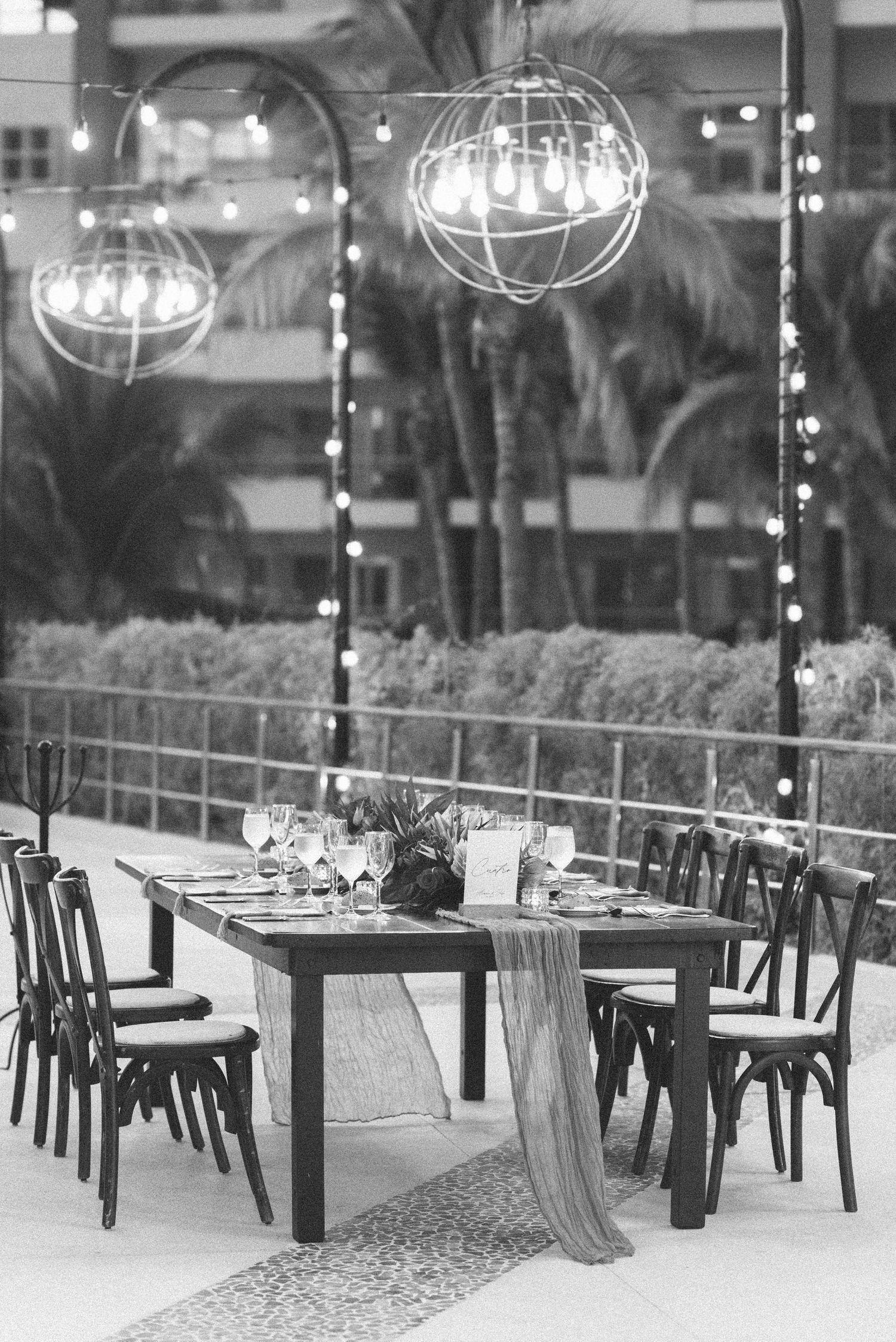 Black and white photo of elegant outdoor dining setup with spherical pendant lights.