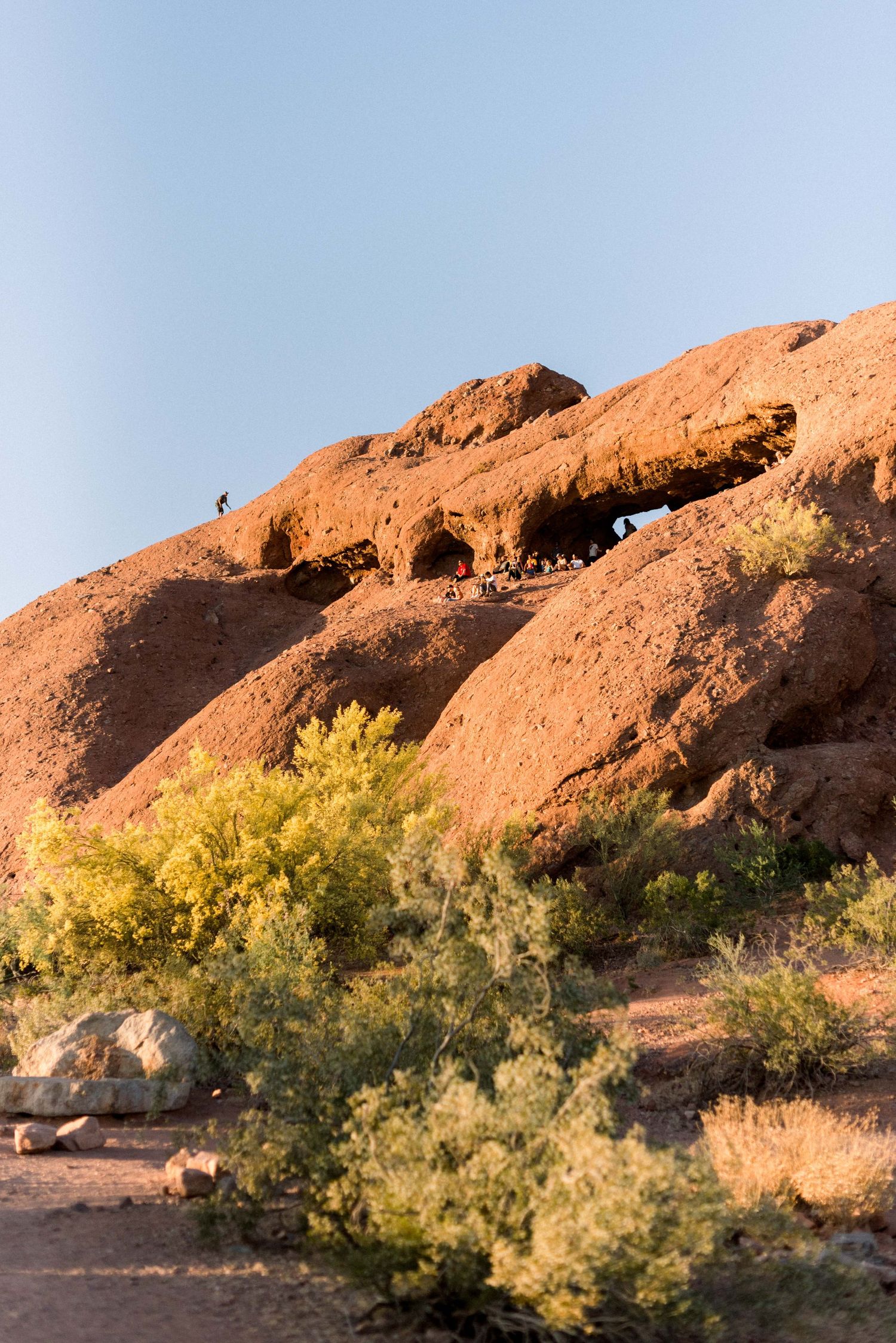 Desert rock formation with natural caves and holes against clear blue sky.