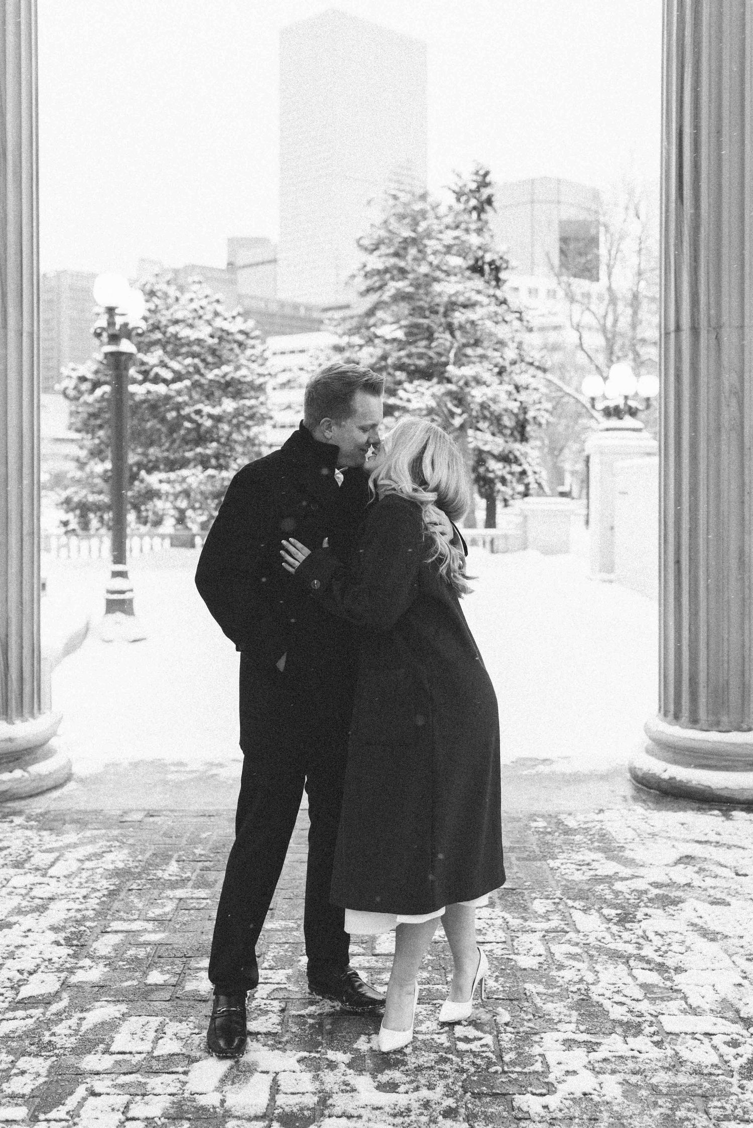 An intimate black and white photo of a couple sharing a moment between stone columns.