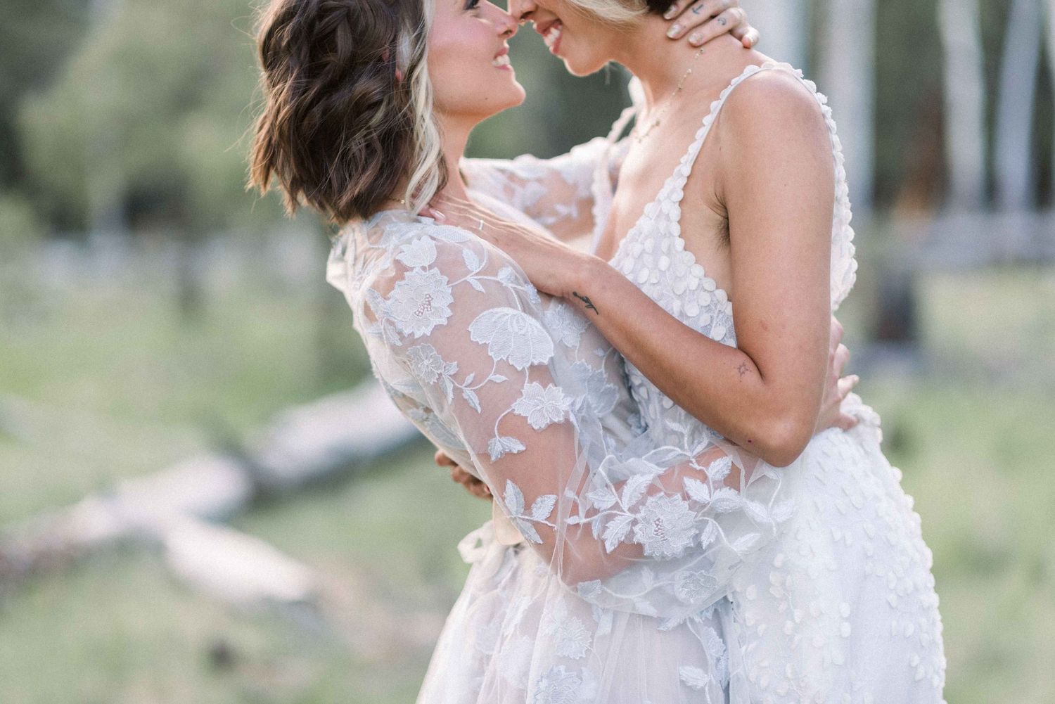 Tender embrace between wedding couple wearing delicate lace gowns outdoors.
