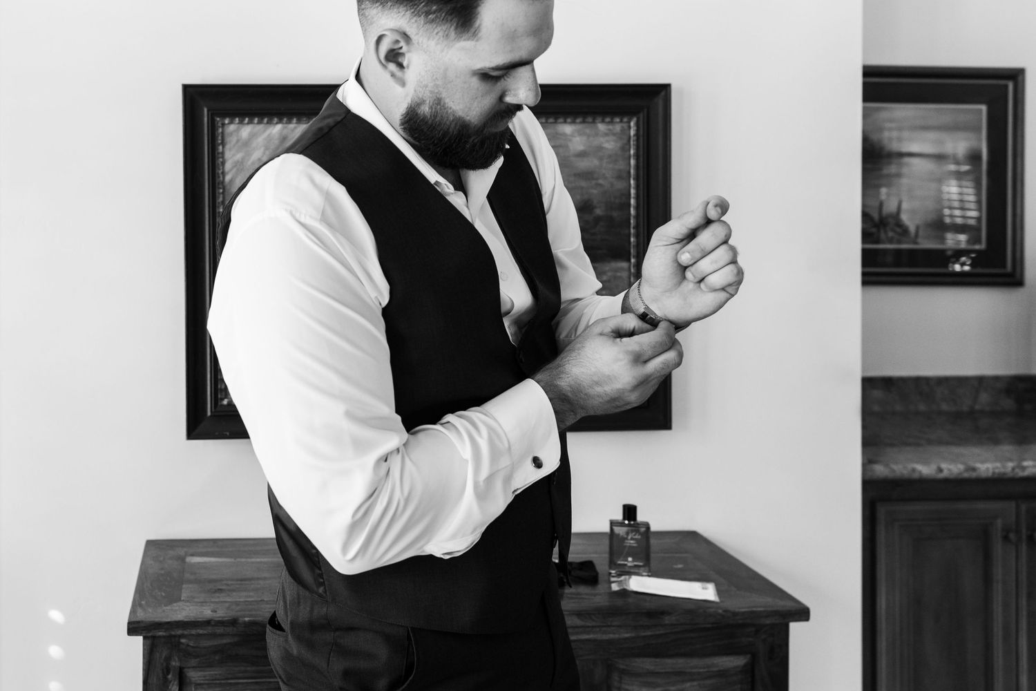 Groom getting ready in formal attire while adjusting cufflinks in black and white.