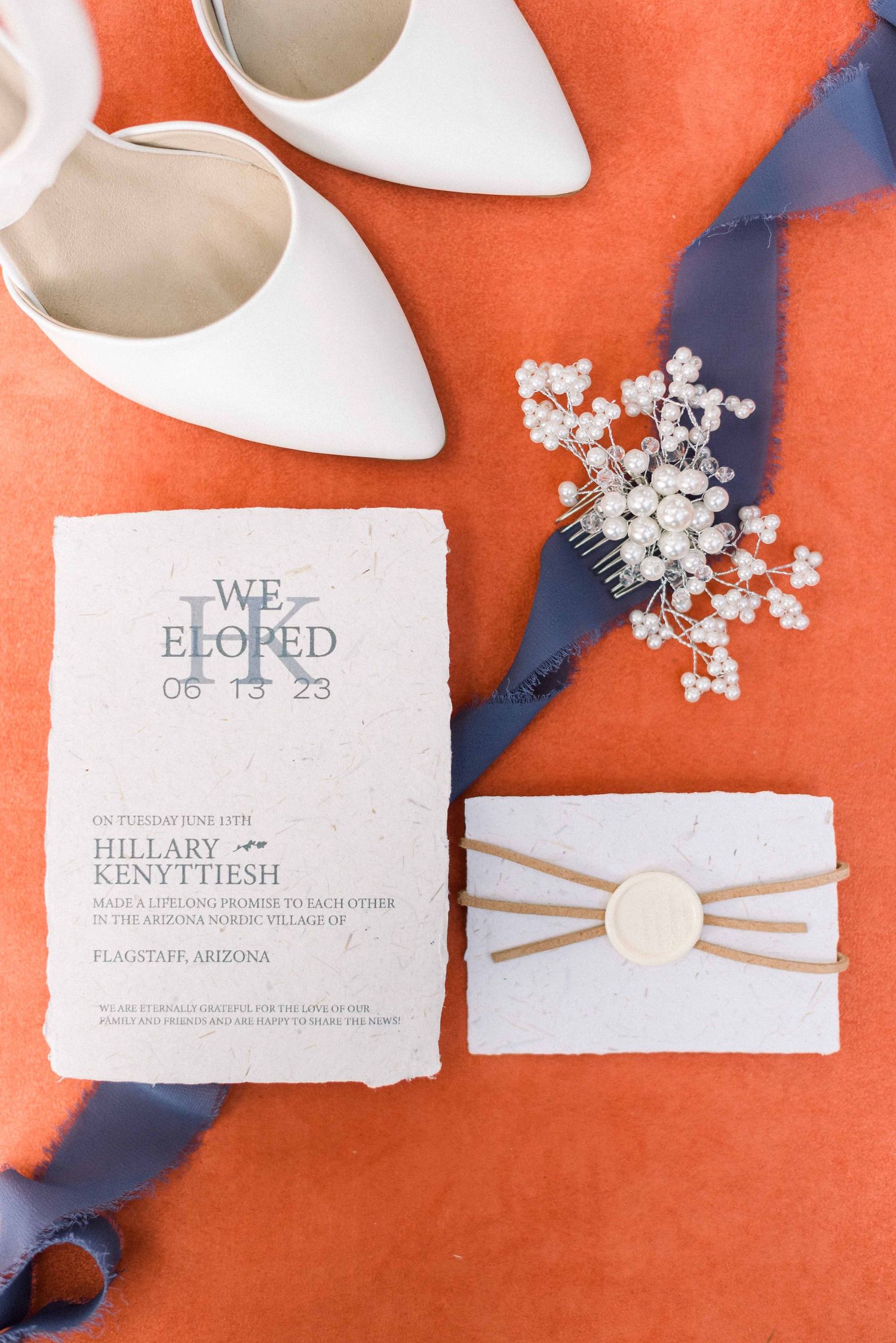 Wedding stationery layout with white shoes, elopement invitation, and floral hair accessories on coral background.