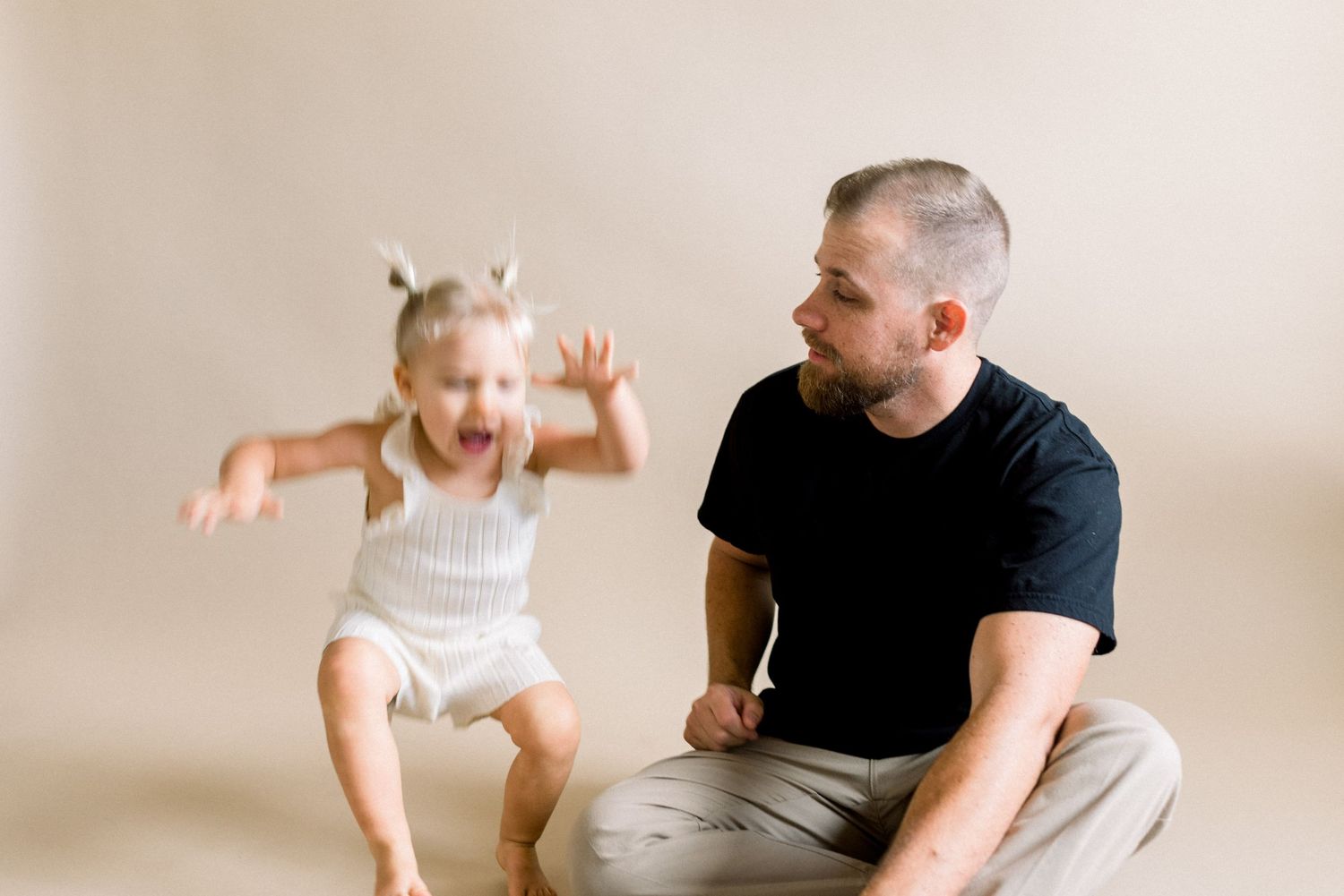Parent and small child sharing a joyful moment during a photo session on beige background.